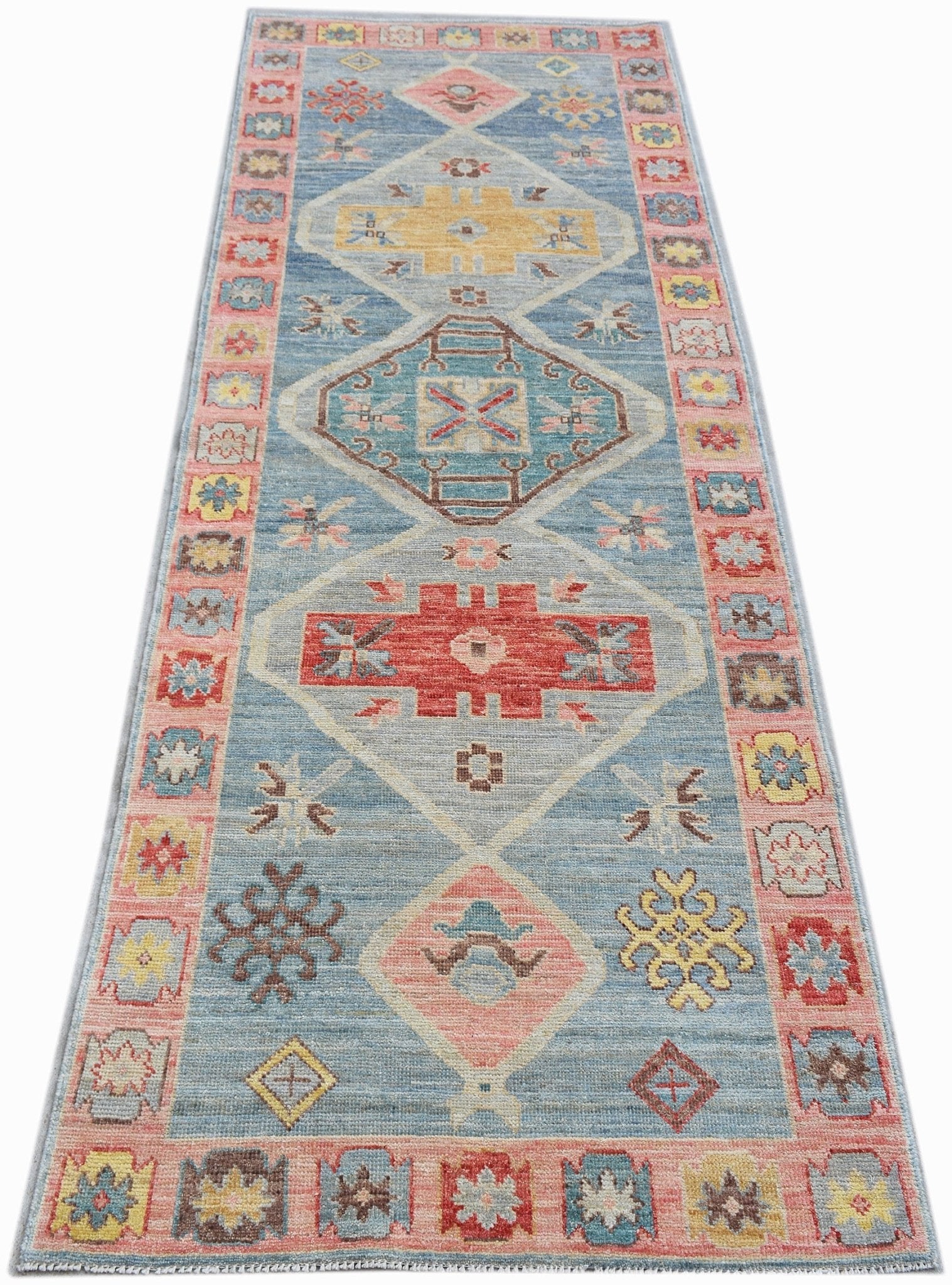 A handwoven transitional Oushak runner rug featuring geometric patterns in blue, pink, and yellow.