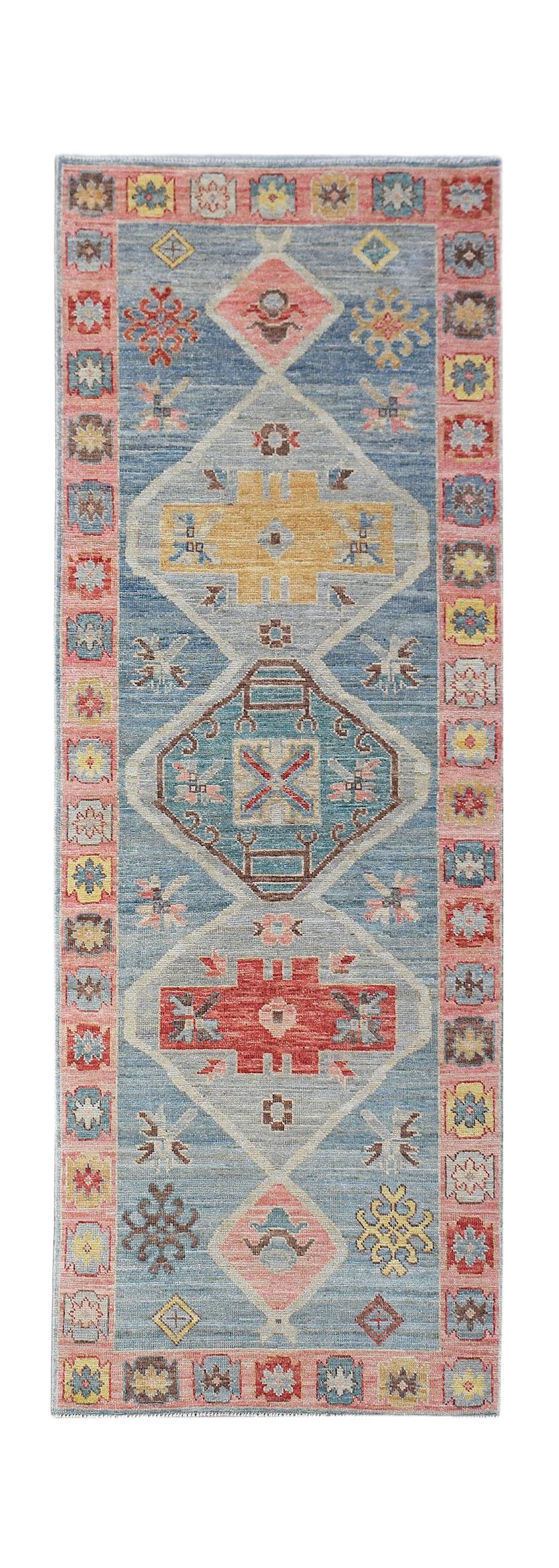 A handwoven wool runner rug featuring a blue field with geometric diamond motifs and pink borders.