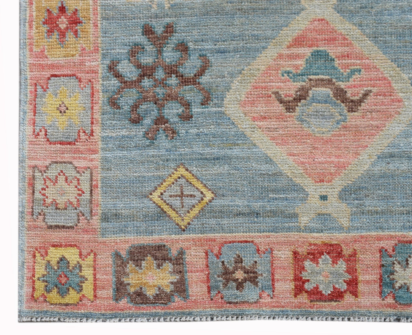 A handwoven wool runner featuring a blue field with pink diamond motifs and floral borders.