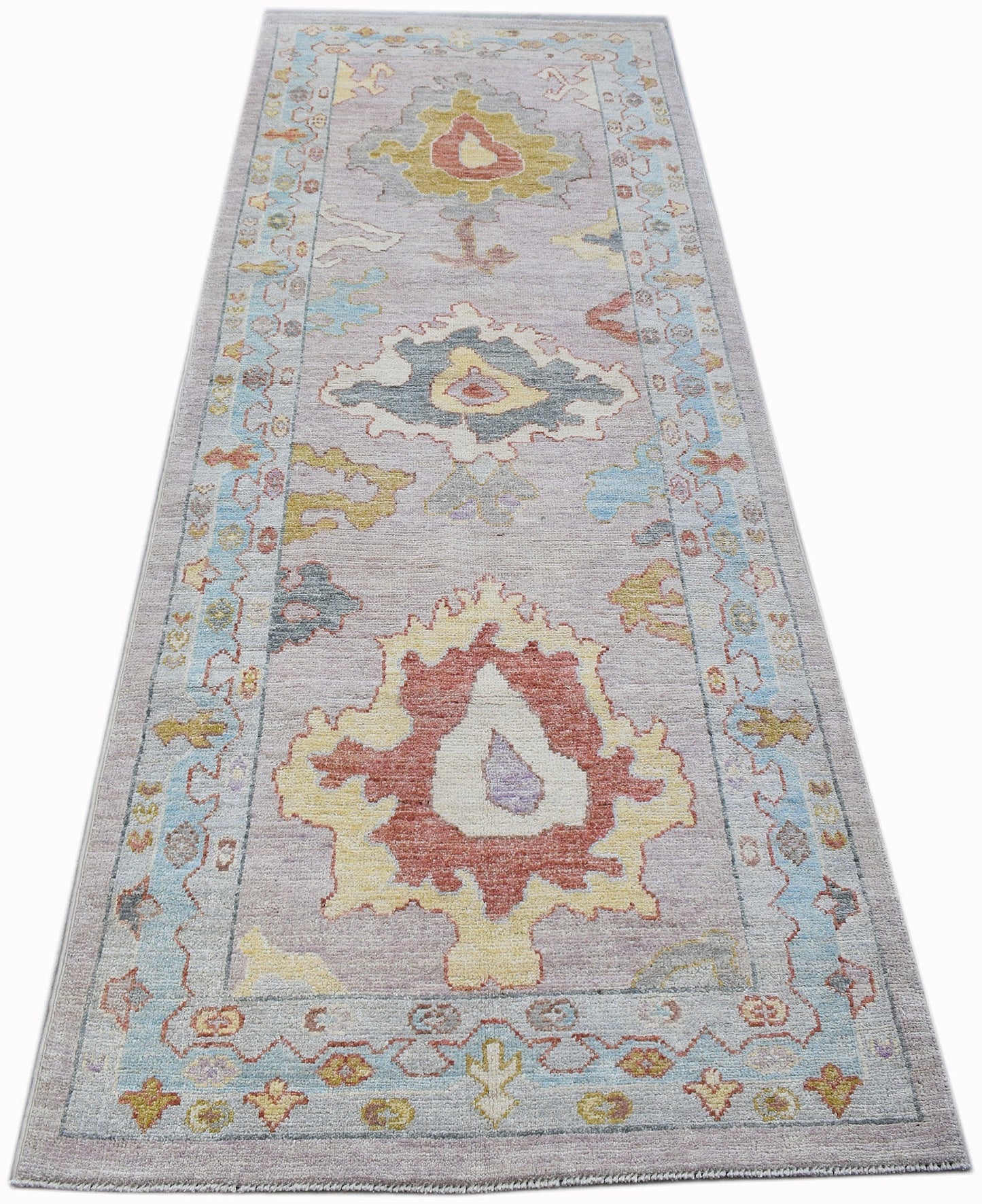 A handwoven wool runner rug featuring a transitional Oushak floral pattern in soft pastel tones.