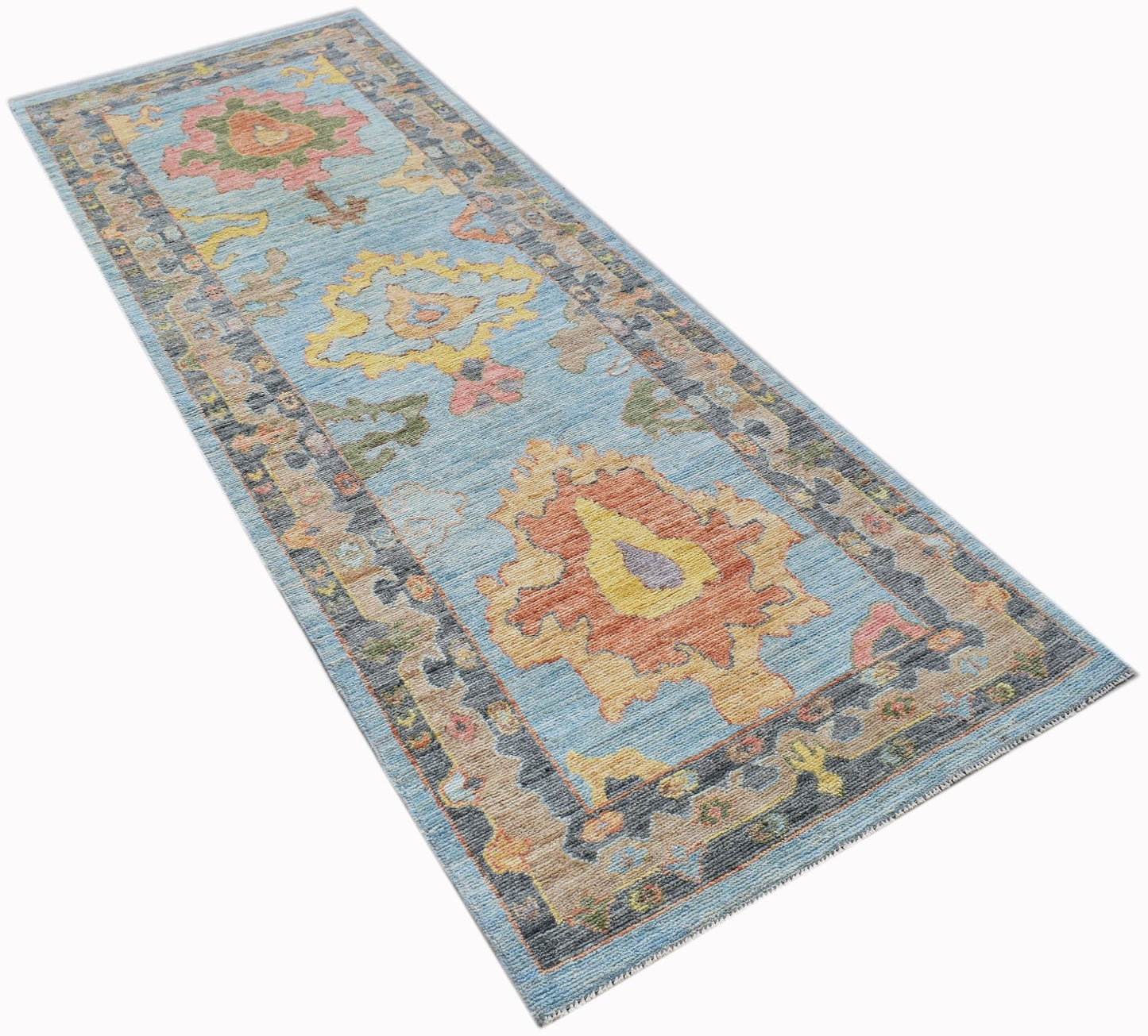 A handwoven wool runner rug featuring a light blue field with colorful floral Oushak patterns.