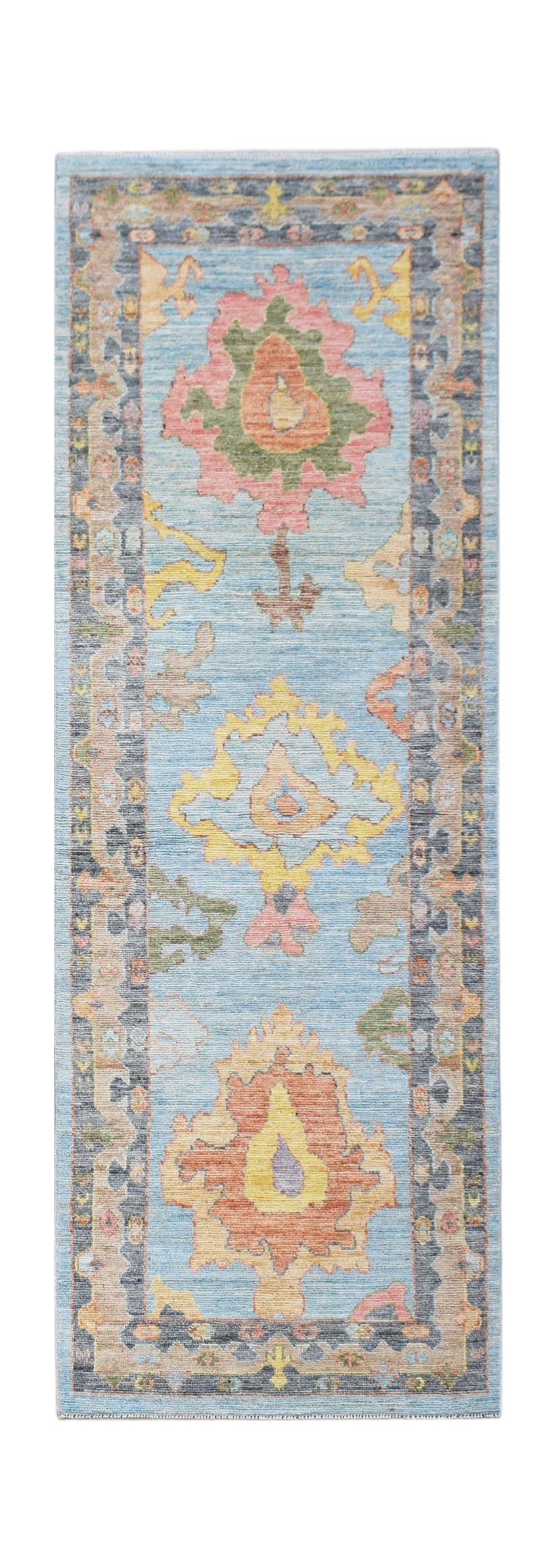 A handwoven wool runner rug featuring a light blue field with colorful floral Oushak motifs.