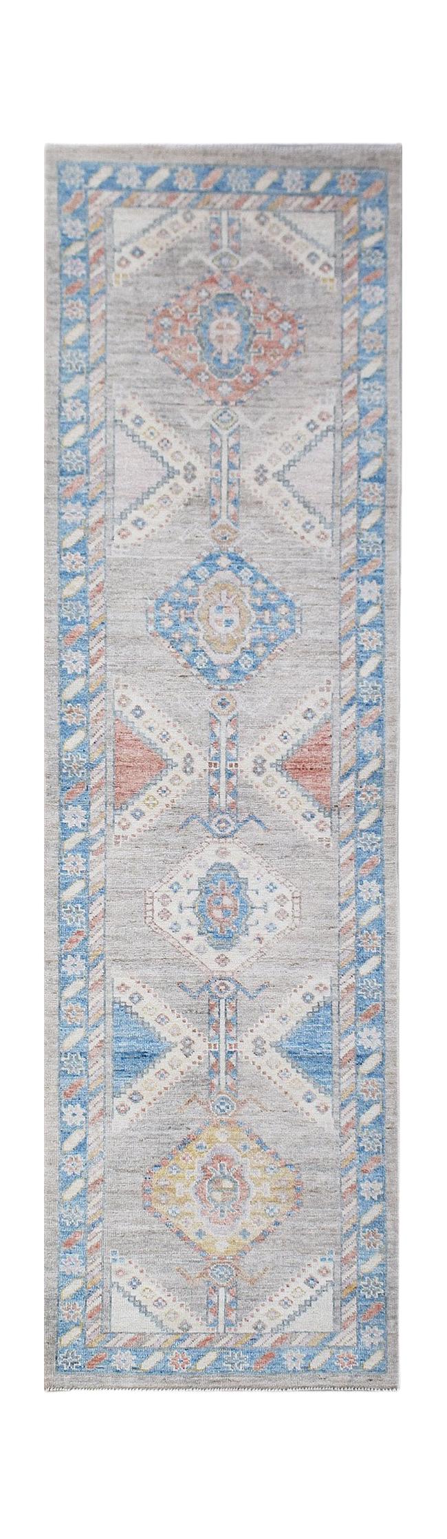 A handwoven wool runner rug featuring a transitional Oushak pattern in blue, grey, and peach tones.