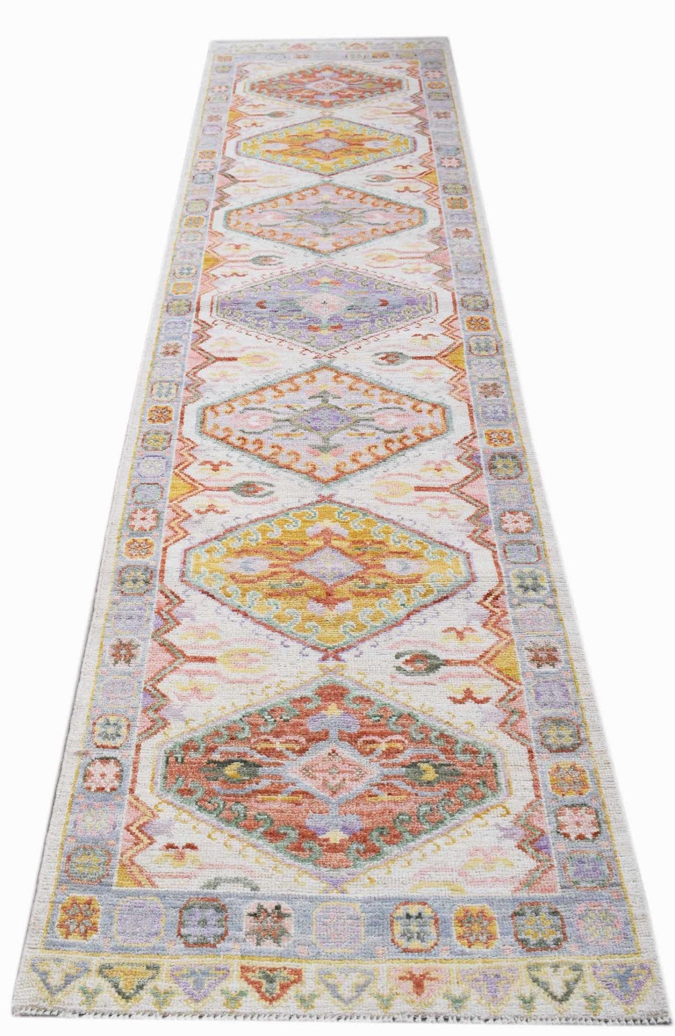 A handwoven wool runner rug featuring a series of colorful diamond medallions on a light background.