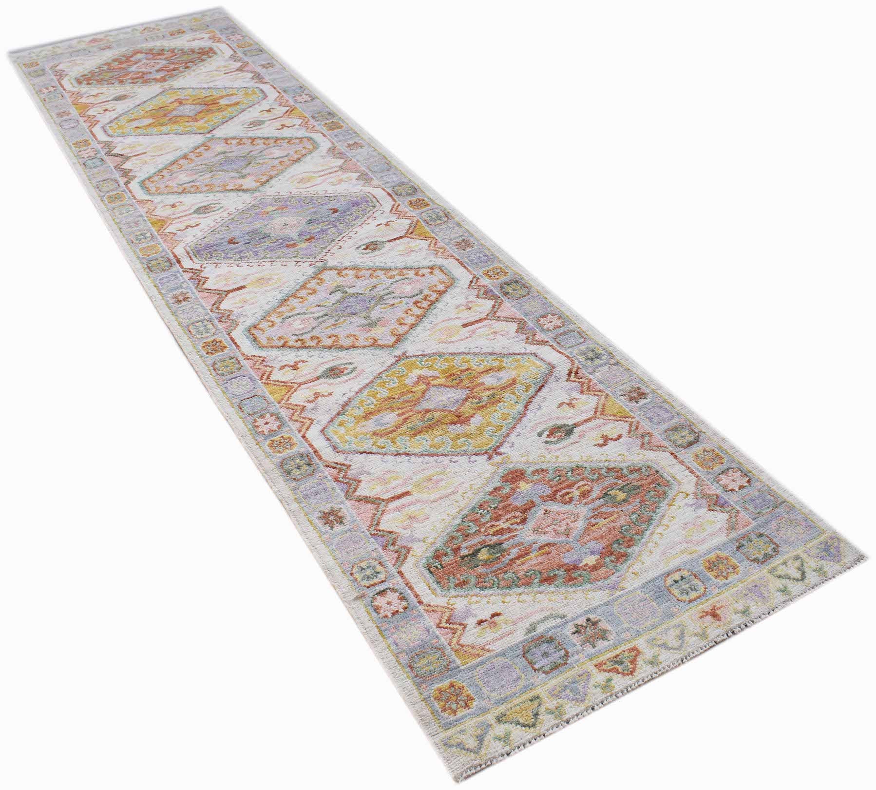 A handwoven wool runner rug featuring a transitional Oushak pattern in soft, multi-colored tones.