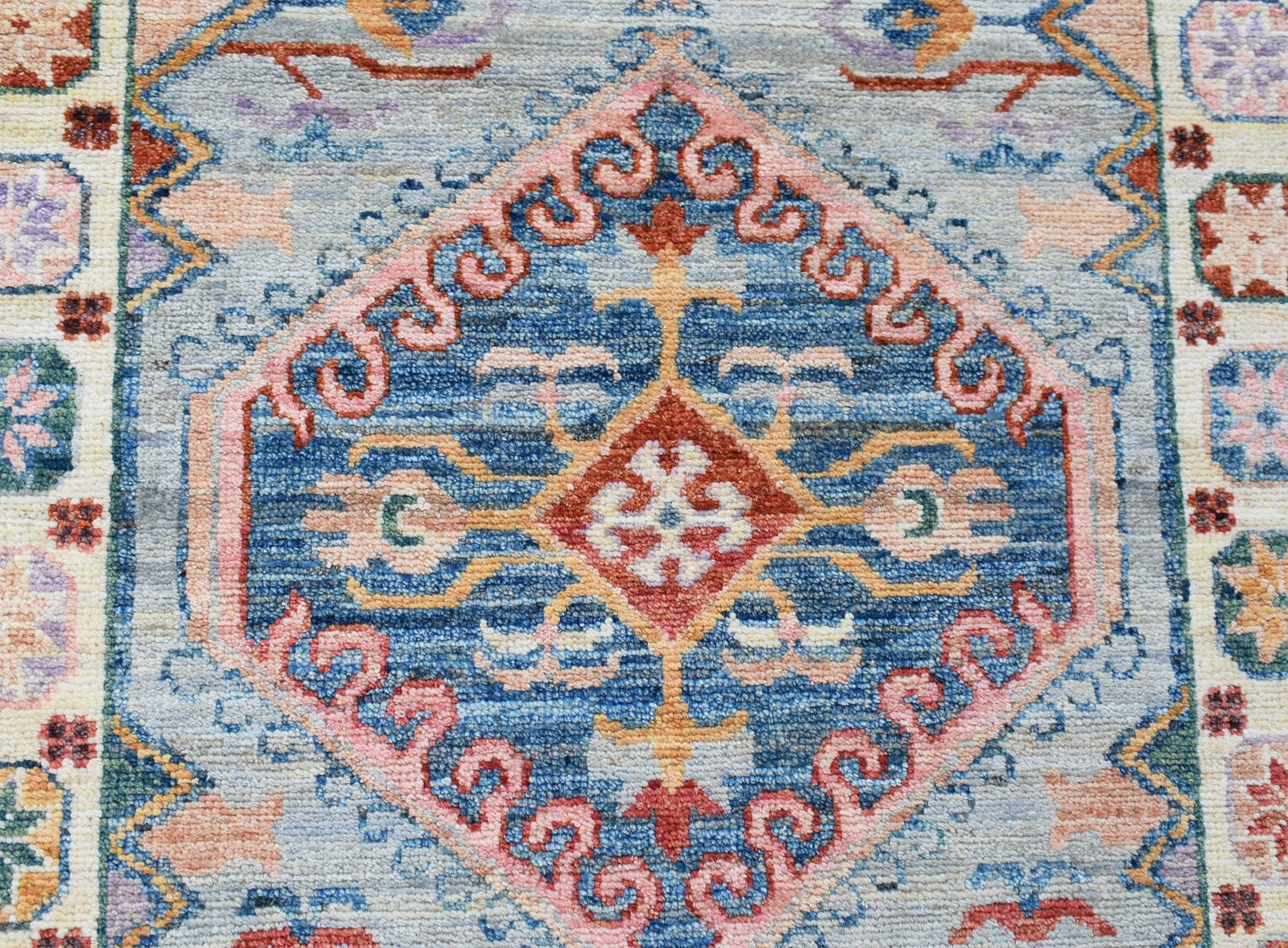 A handwoven wool runner rug featuring a central blue diamond medallion with pink and orange motifs.