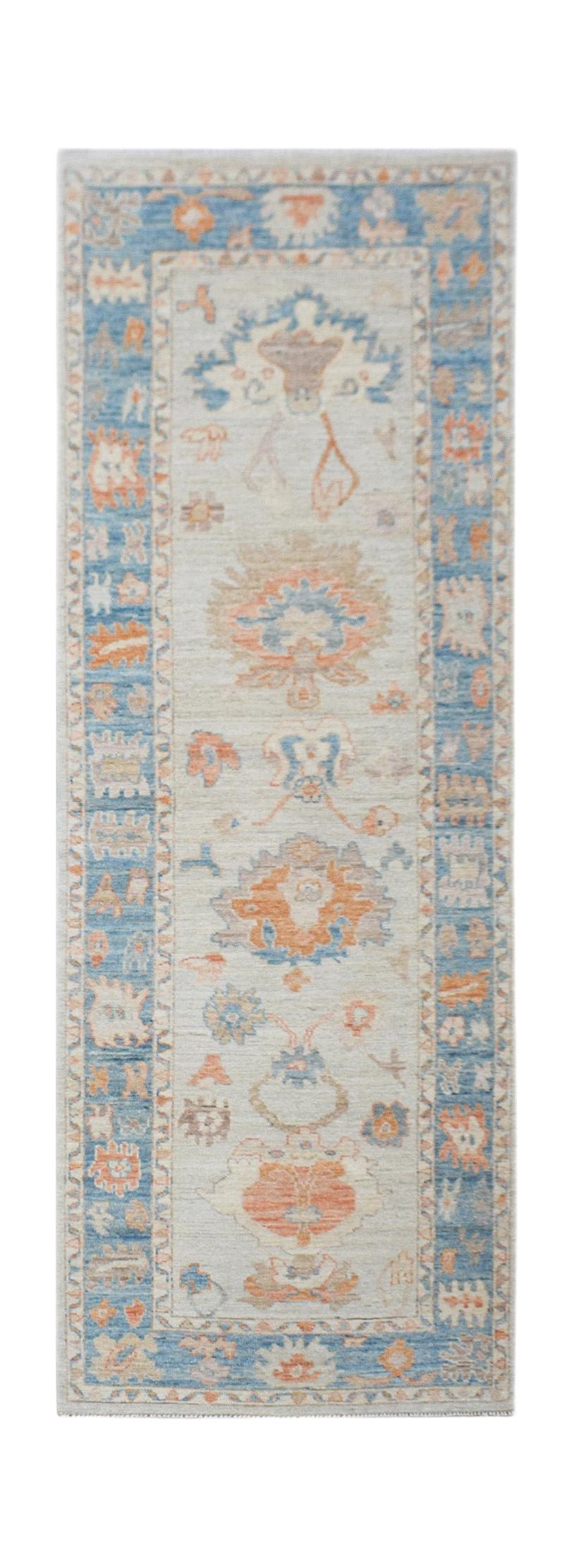 A handwoven wool runner rug featuring a transitional floral pattern in blue and orange tones.