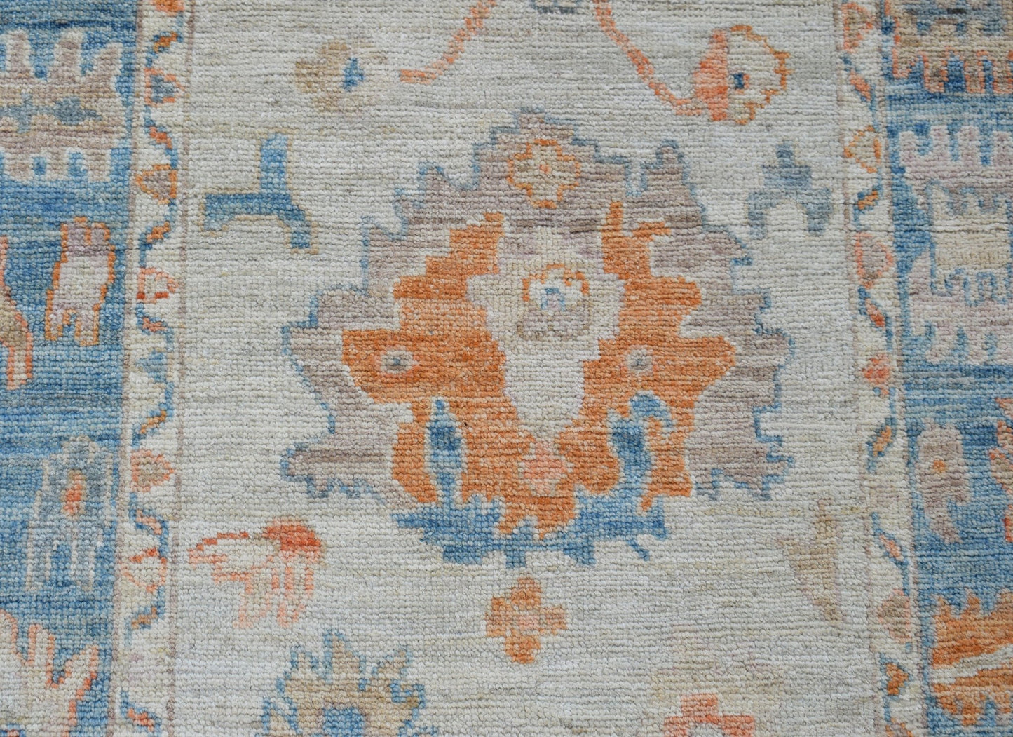 A handwoven wool runner featuring a transitional floral pattern in orange, blue, and beige tones.
