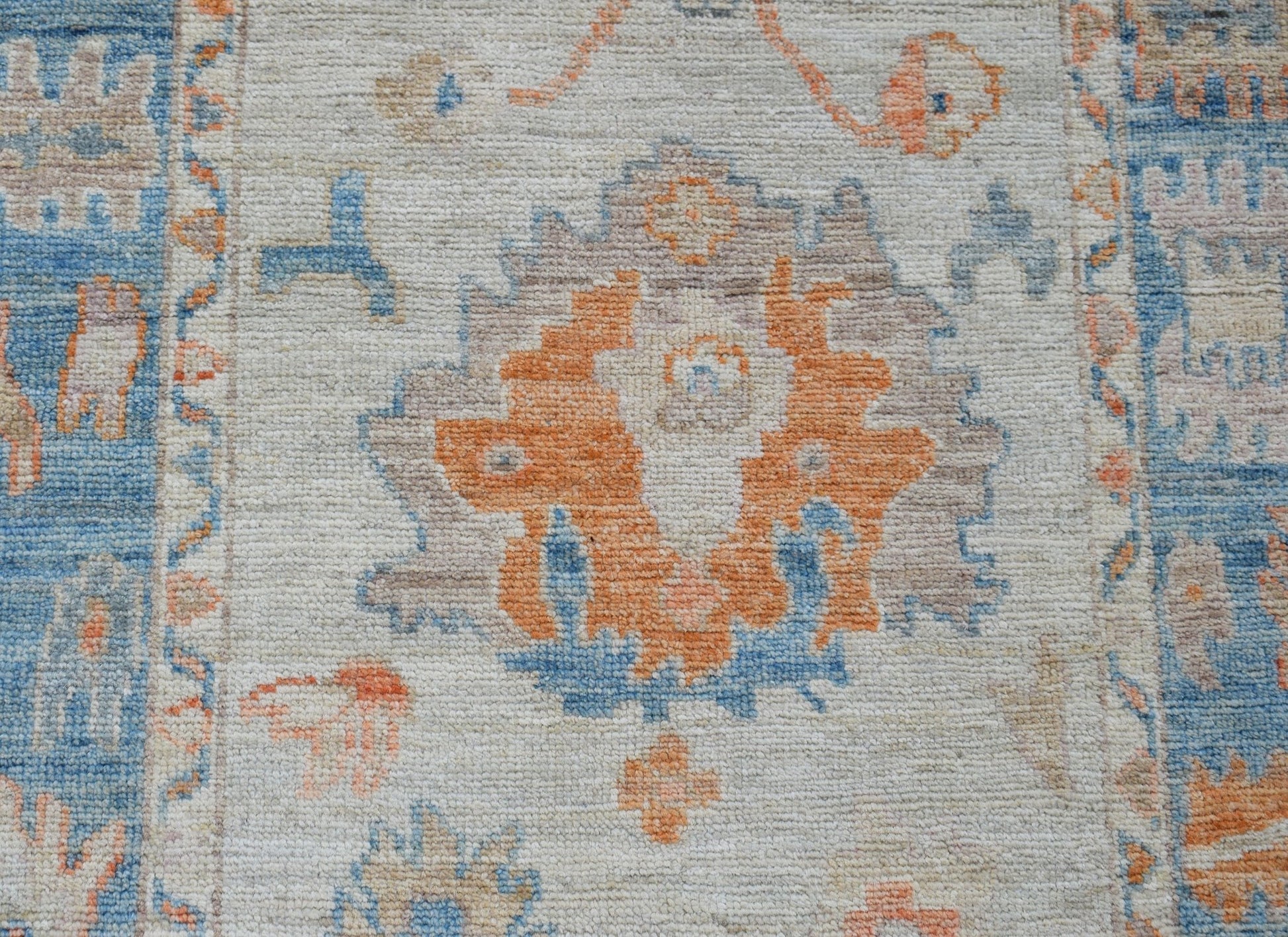 A handwoven wool runner featuring a transitional floral pattern in orange, blue, and beige tones.