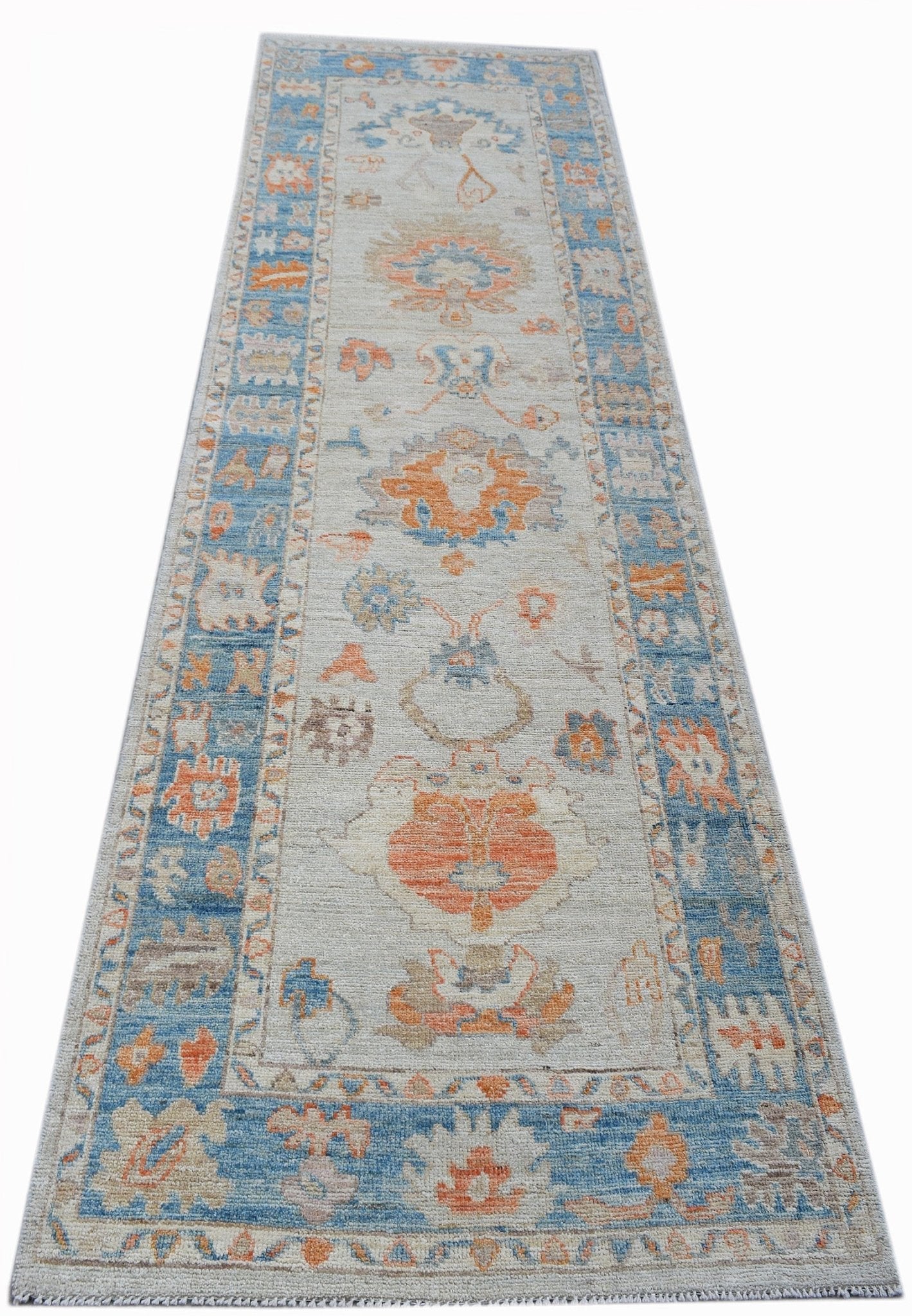 A handwoven wool runner rug featuring a transitional floral pattern in blue and orange tones.