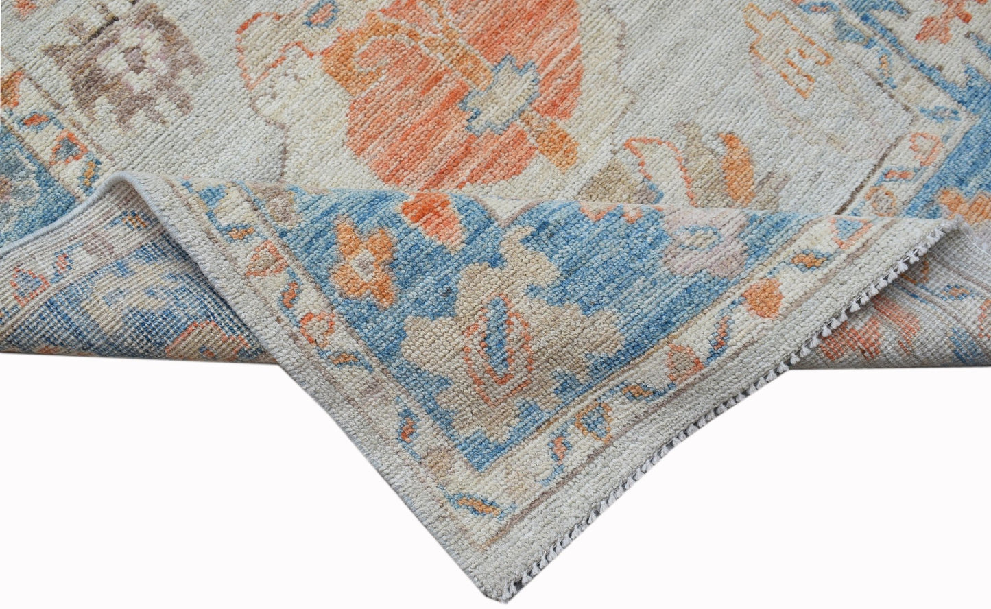 A handwoven wool runner featuring a transitional floral pattern in blue, orange, and cream tones.