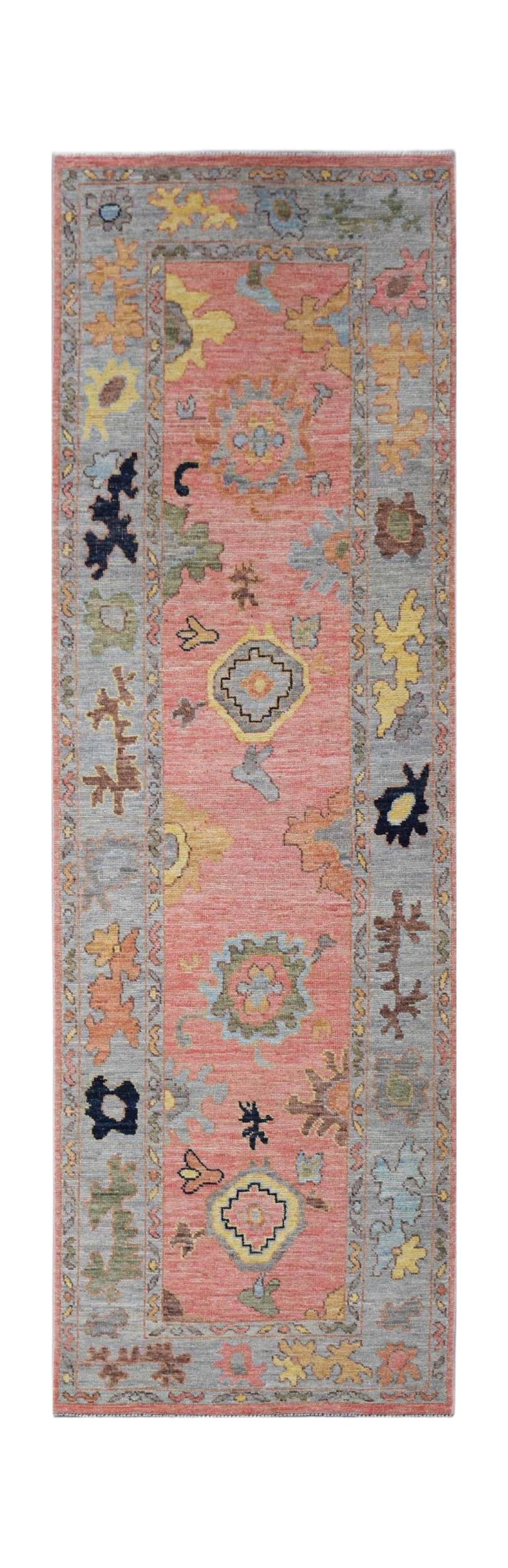 A handwoven Oushak runner rug featuring a floral pattern in pink, grey, and yellow tones.