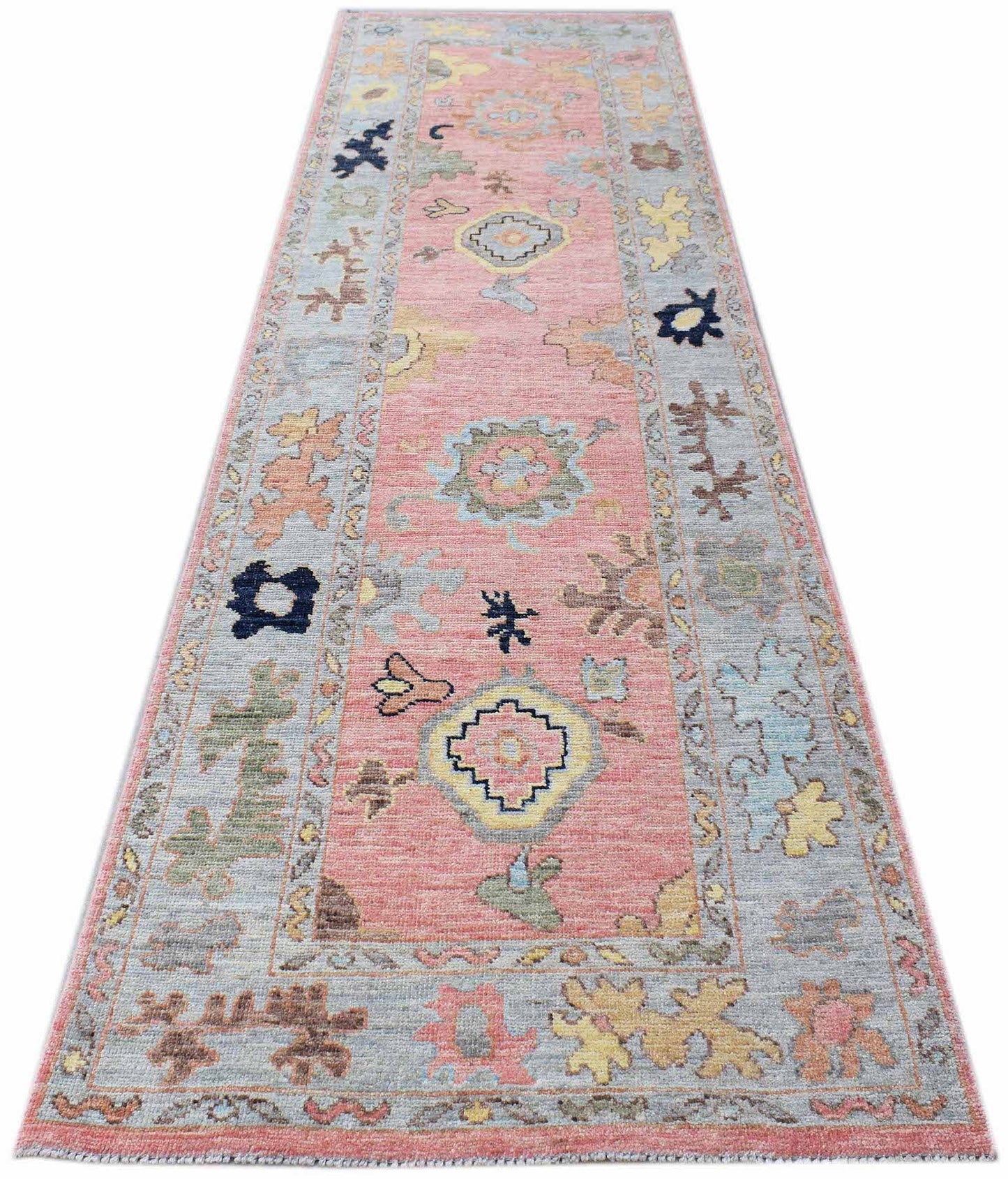 A handwoven wool runner rug featuring a transitional floral pattern in pink and blue tones.