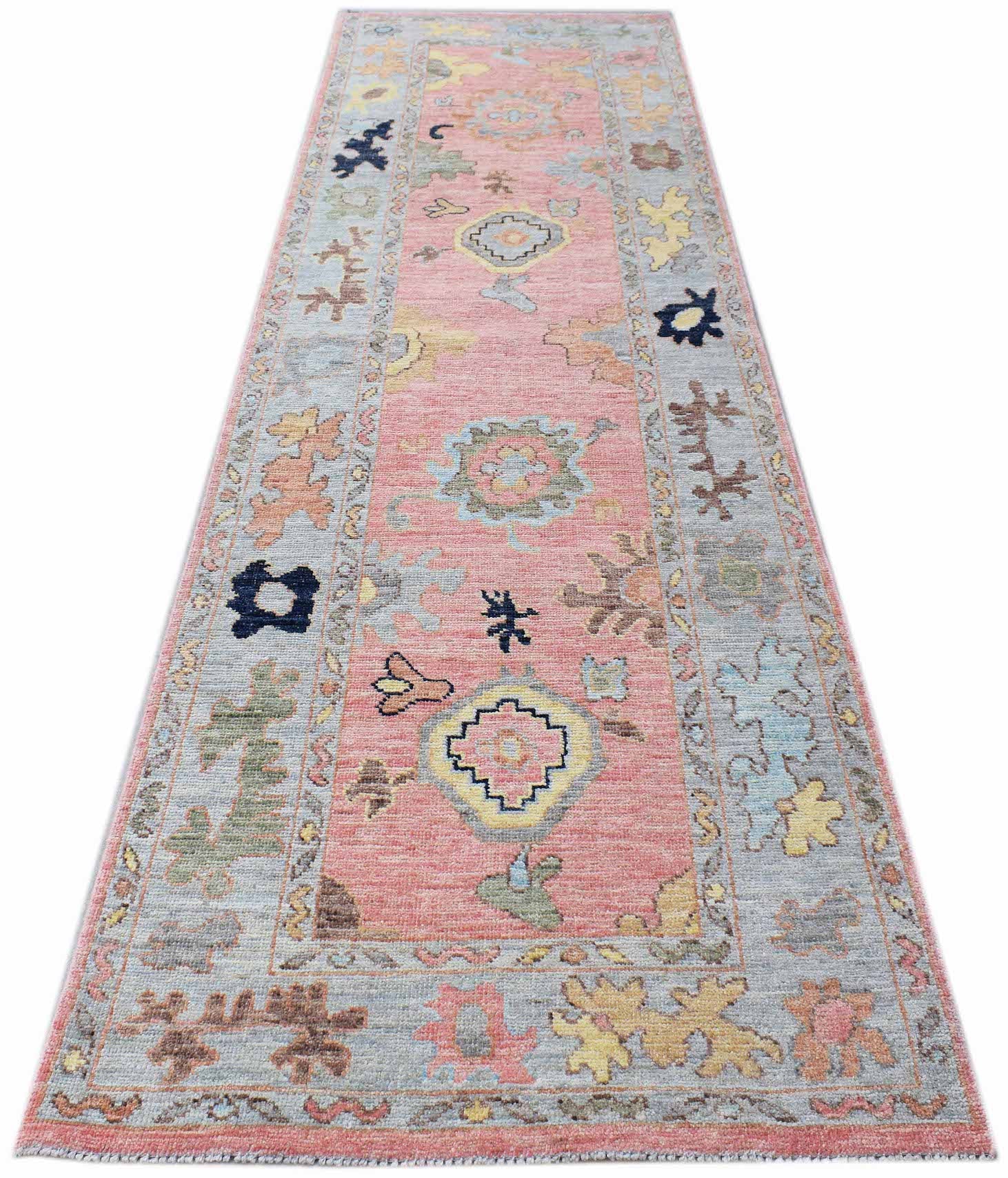 A handwoven wool runner rug featuring a transitional floral pattern in pink and blue tones.