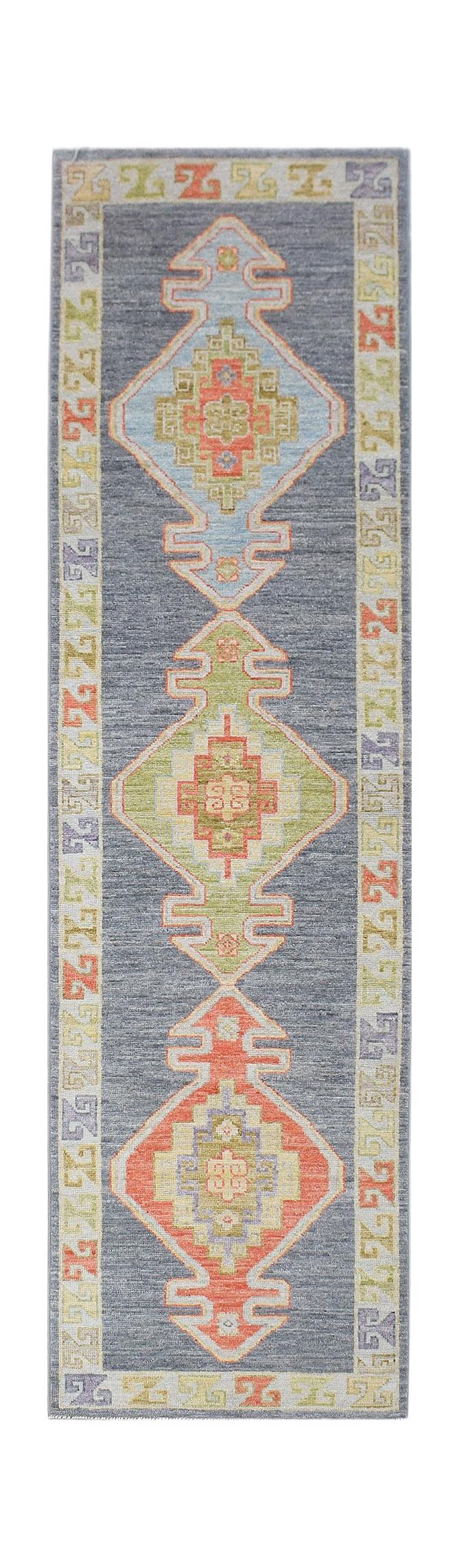 A handwoven wool runner rug featuring three geometric diamond medallions on a dark grey field.