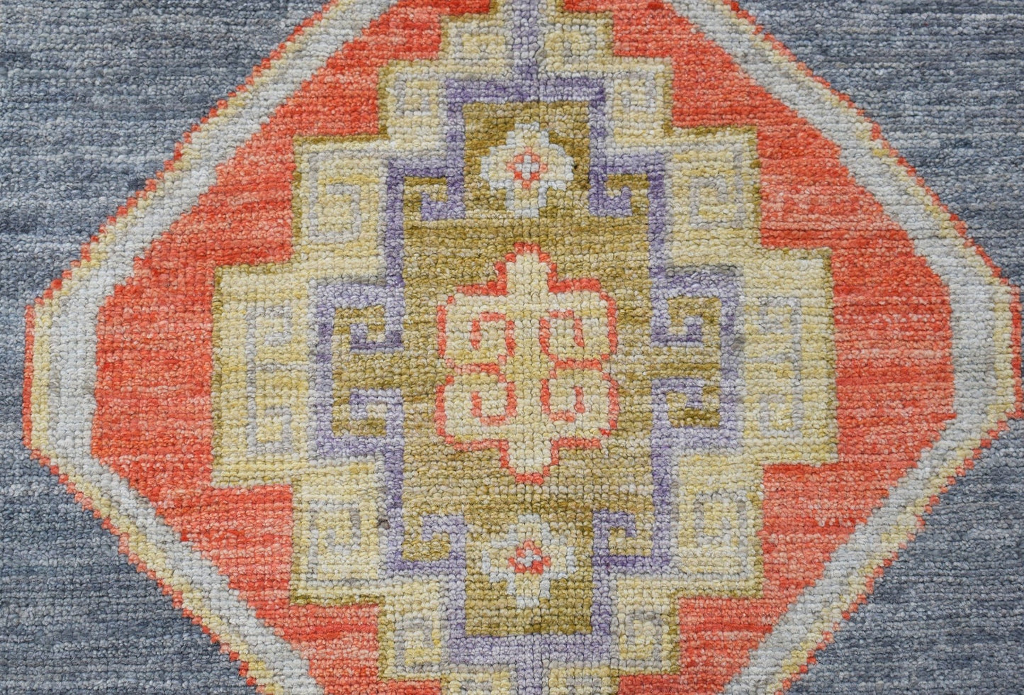 A handwoven Oushak runner featuring a geometric medallion in orange, purple, and gold on blue.