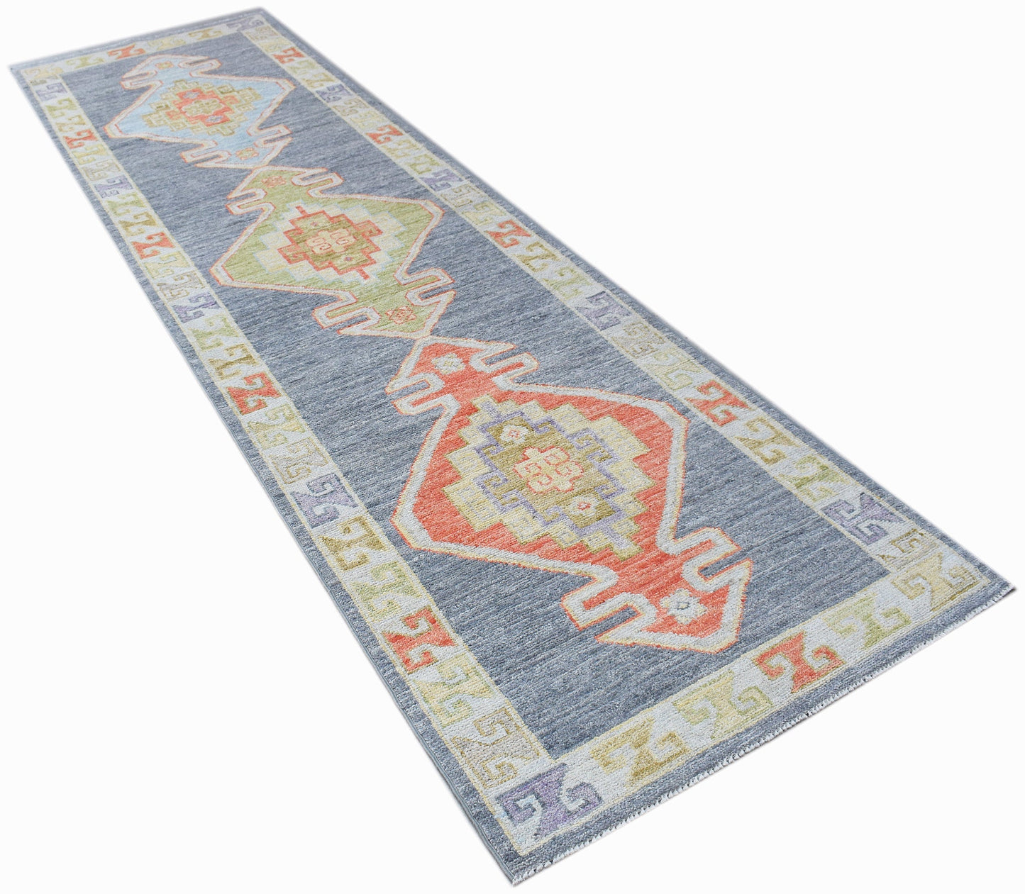 A handwoven wool runner rug featuring a blue background with colorful geometric Oushak patterns.