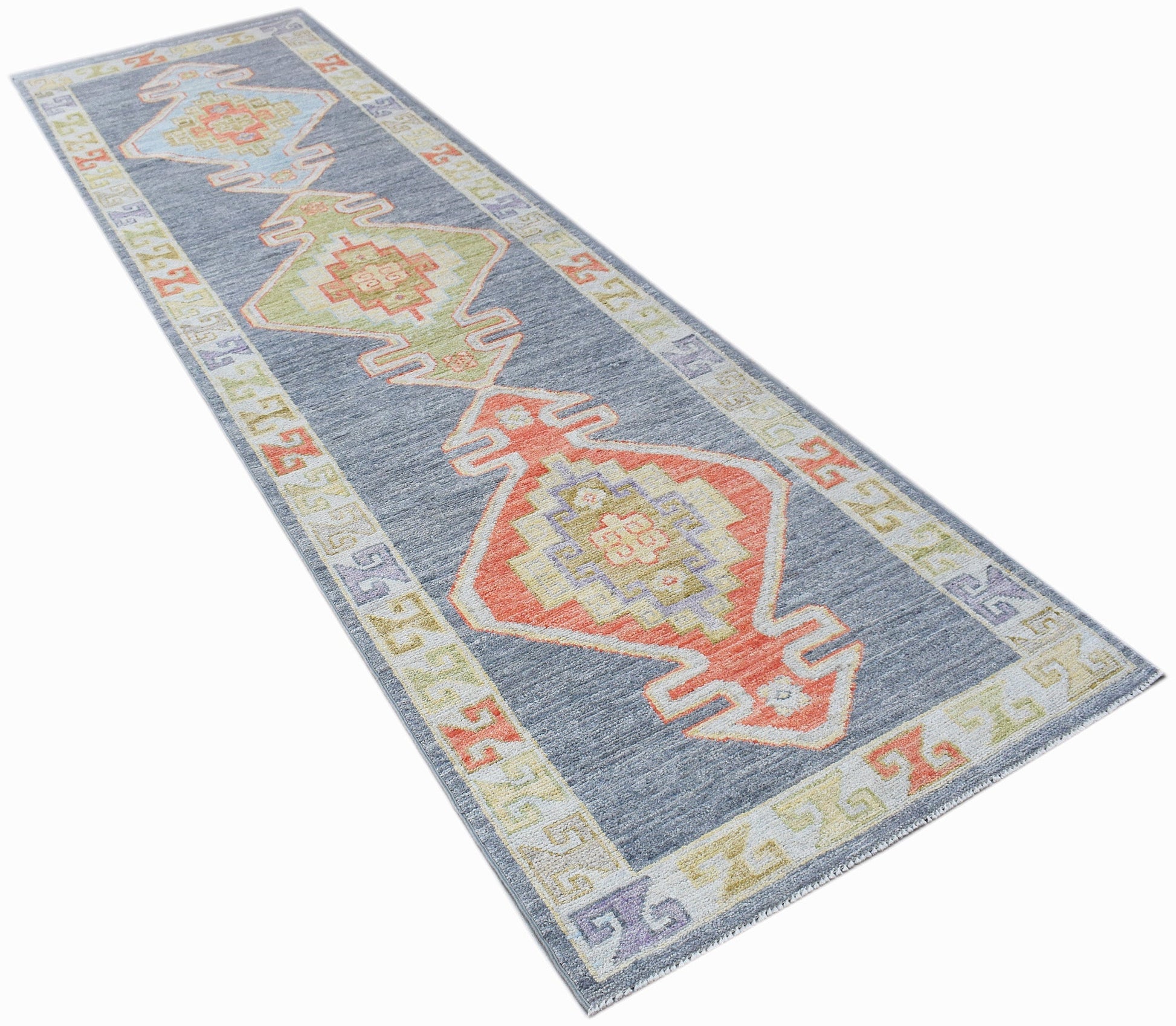 A handwoven wool runner rug featuring a blue background with colorful geometric Oushak patterns.
