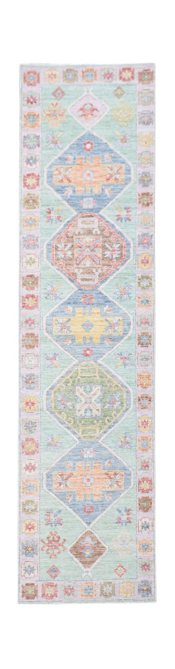 A handwoven wool runner rug featuring a light green background with colorful geometric medallions.