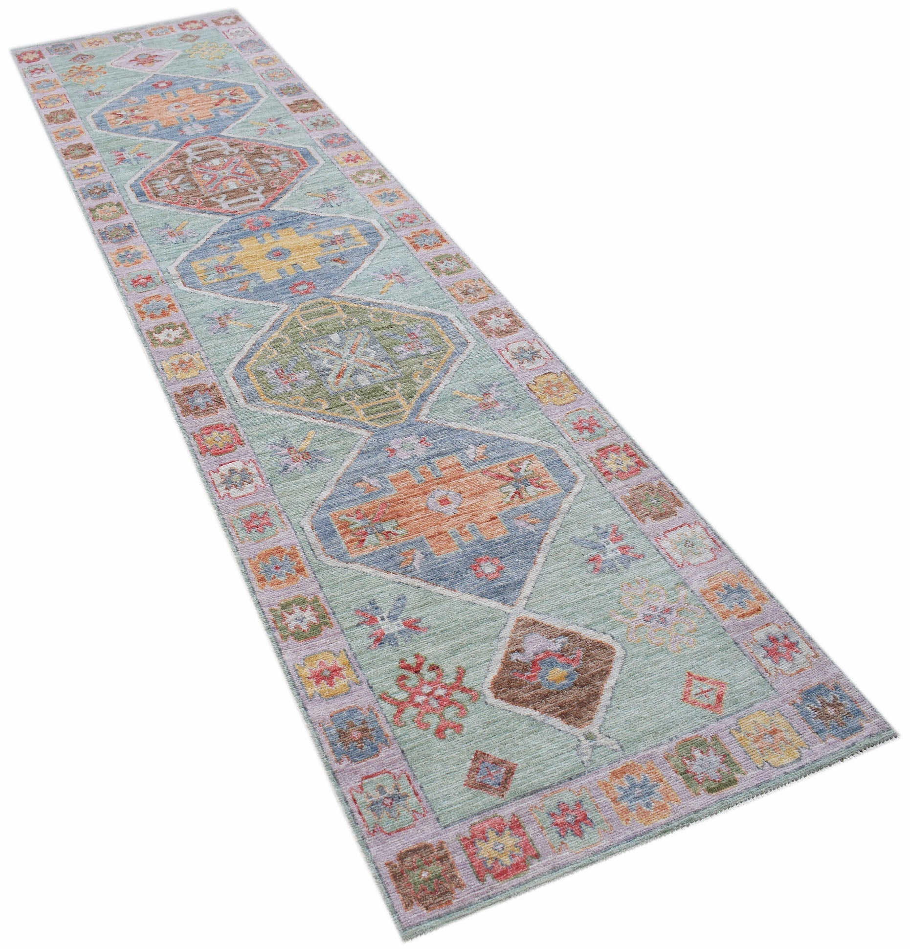 A handwoven wool runner rug featuring a light blue field with colorful geometric Oushak patterns.