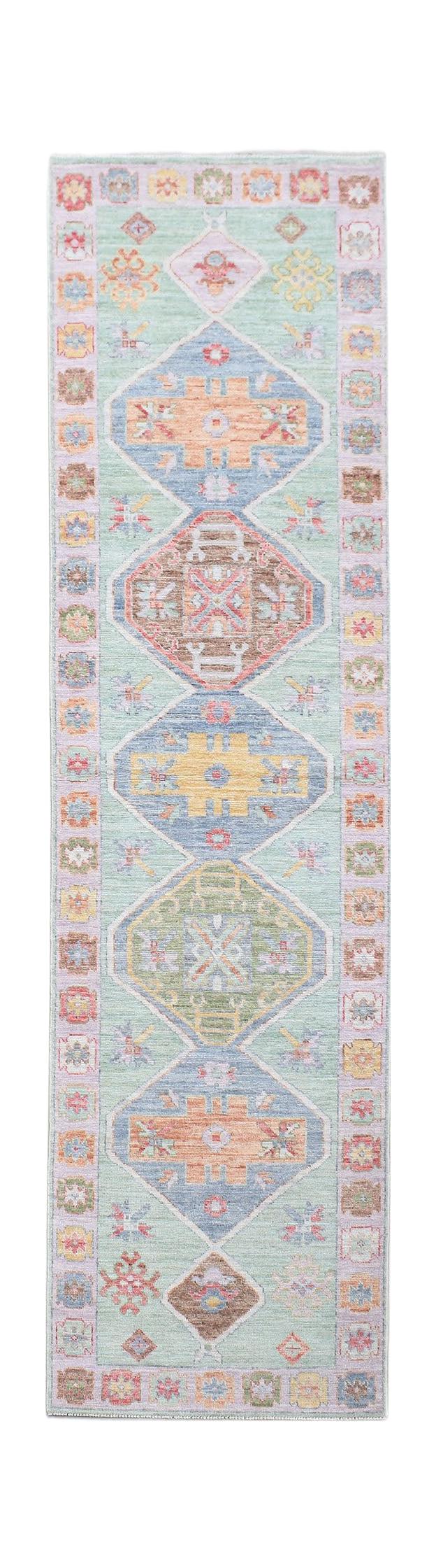 A handwoven wool runner rug featuring a light green field with colorful geometric diamond motifs.