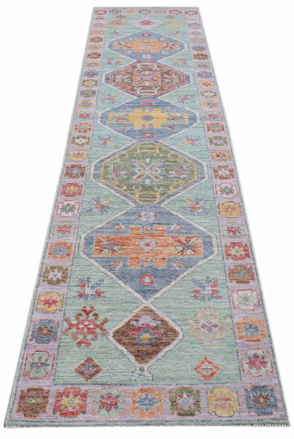 A handwoven wool runner rug featuring a transitional Oushak pattern in soft, multi-colored tones.