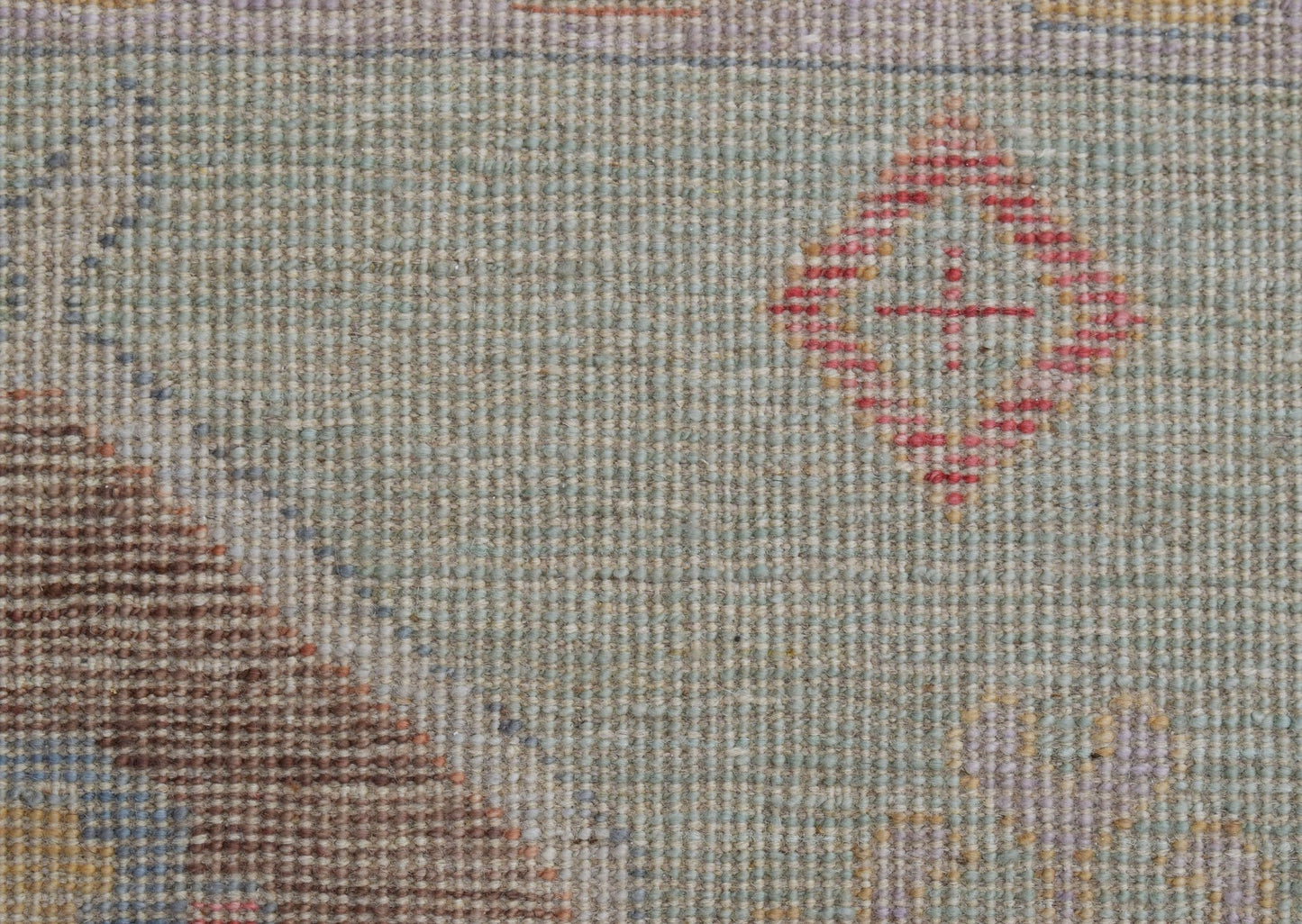 A handwoven wool runner featuring a light green field with a small red diamond motif.