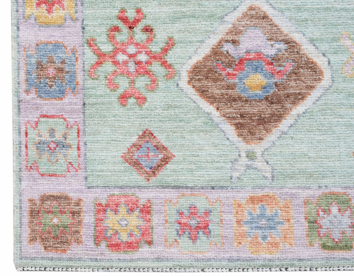 A handwoven wool runner featuring a light green field with geometric floral motifs and a patterned border.