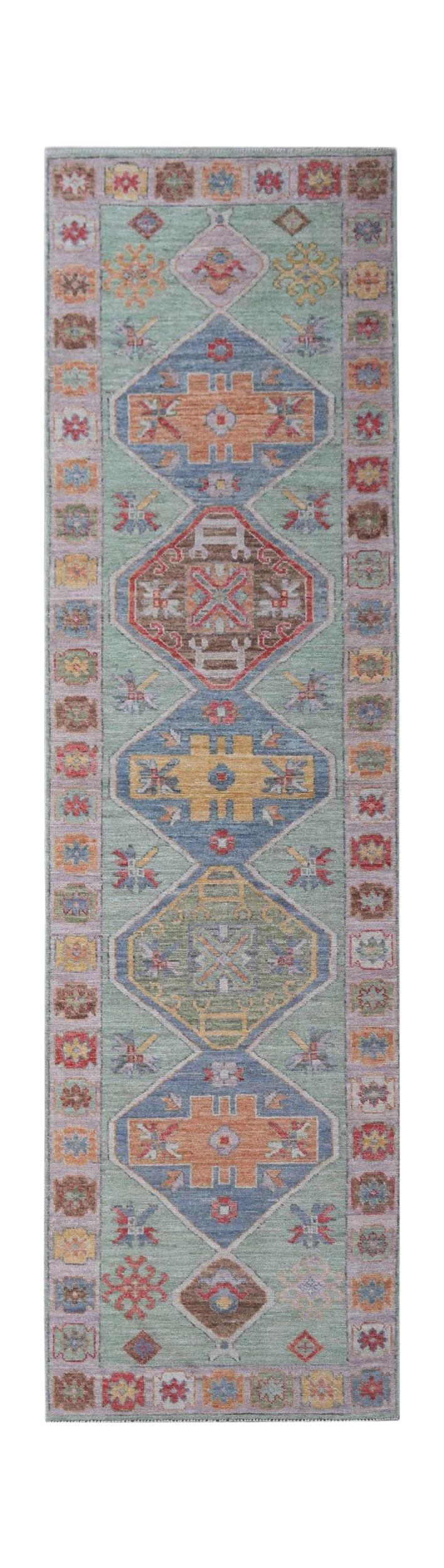 A handwoven wool runner rug featuring a light green field with geometric medallions in muted tones.