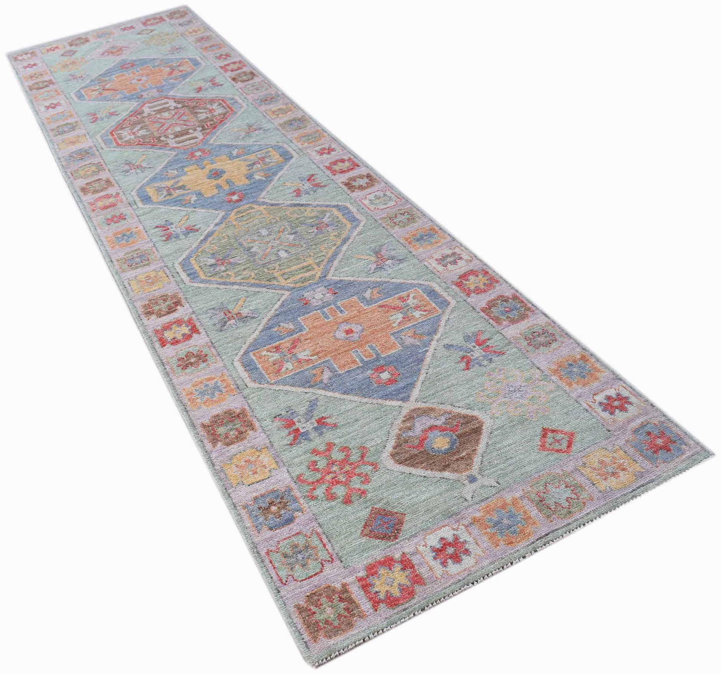 A handwoven wool runner rug featuring a light green field with geometric medallions and floral motifs.