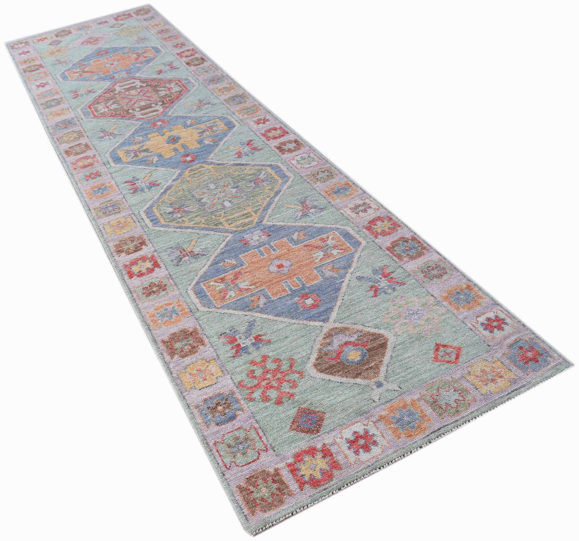 A handwoven wool runner rug featuring a light green field with geometric medallions and floral motifs.