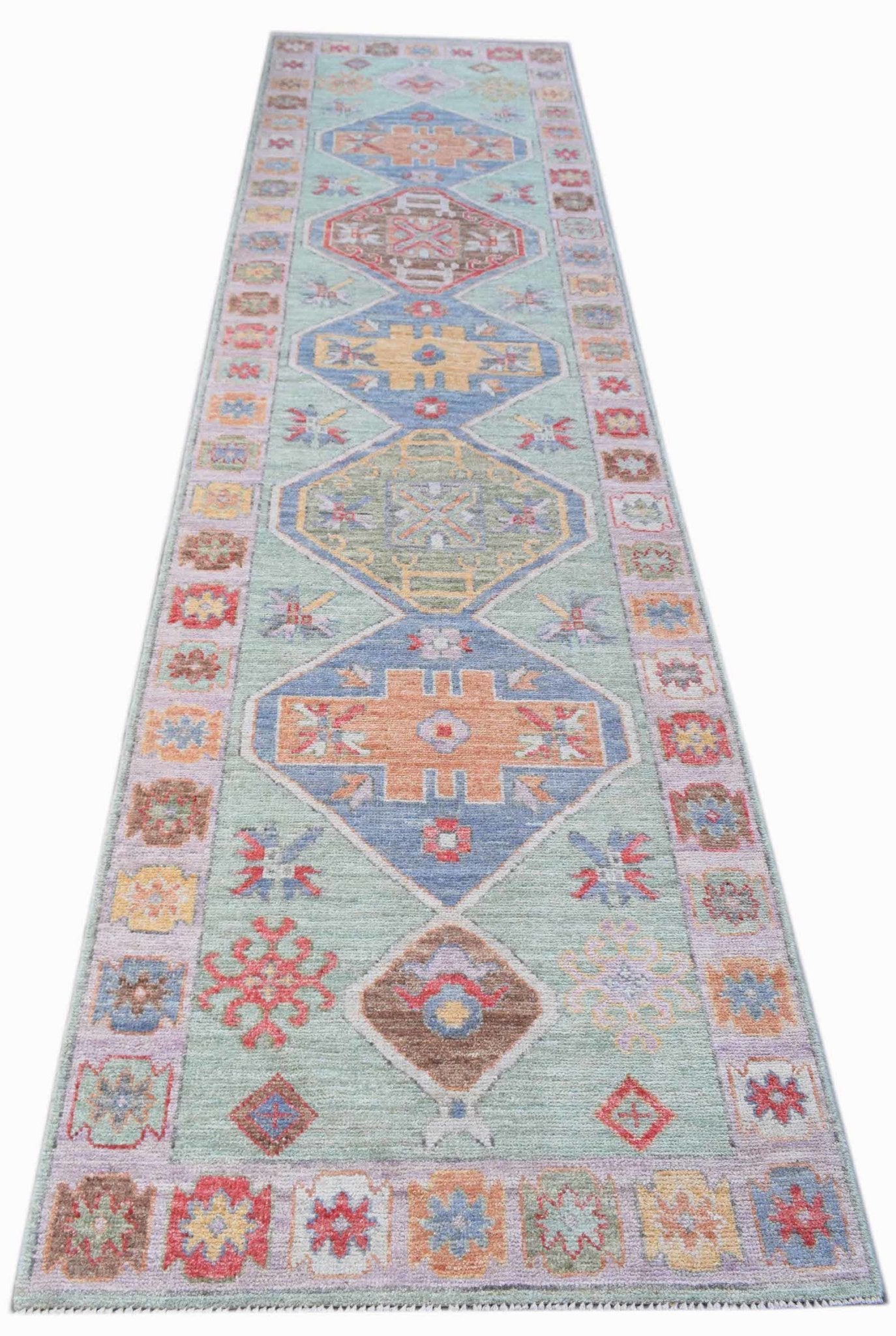 A handwoven wool runner rug featuring a light green field with colorful geometric Oushak motifs.