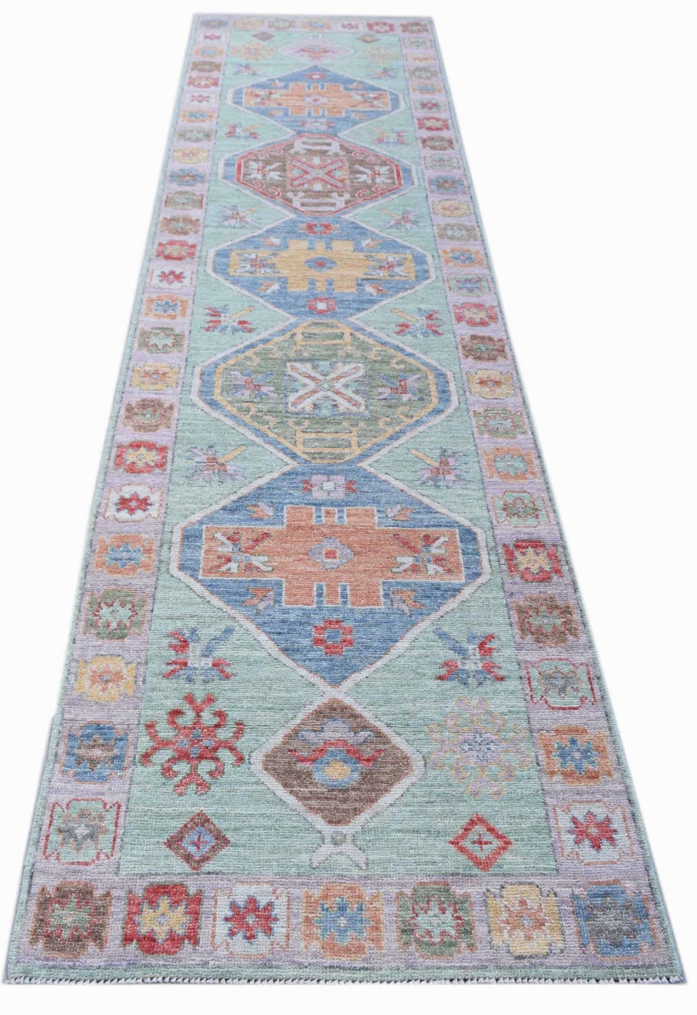 A handwoven transitional Oushak runner featuring geometric medallions on a light green background.
