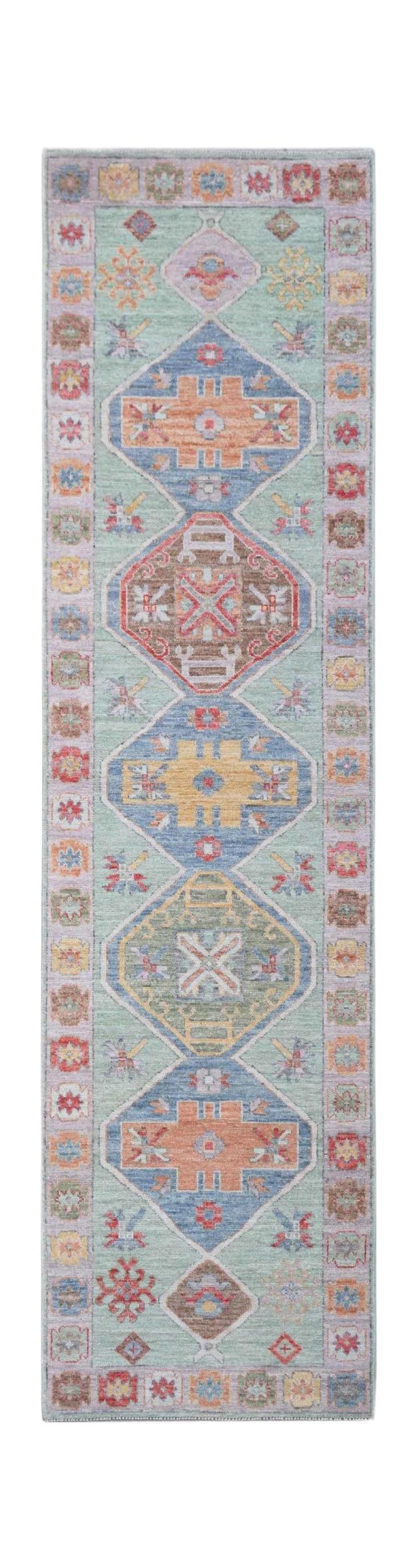 A handwoven wool runner rug featuring a light green field with colorful geometric medallions.