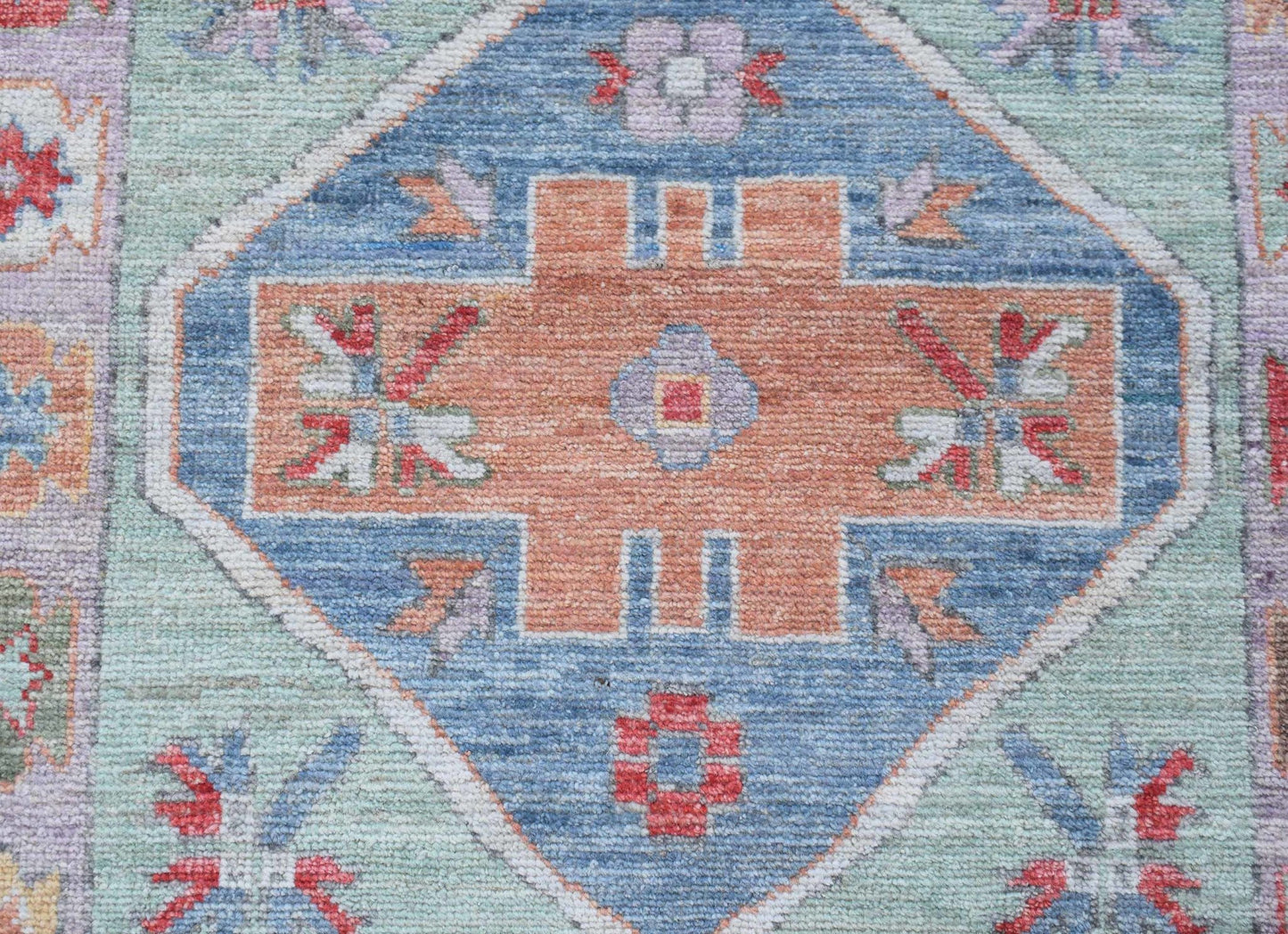 A handwoven wool runner featuring a central orange geometric medallion on a blue and green field.