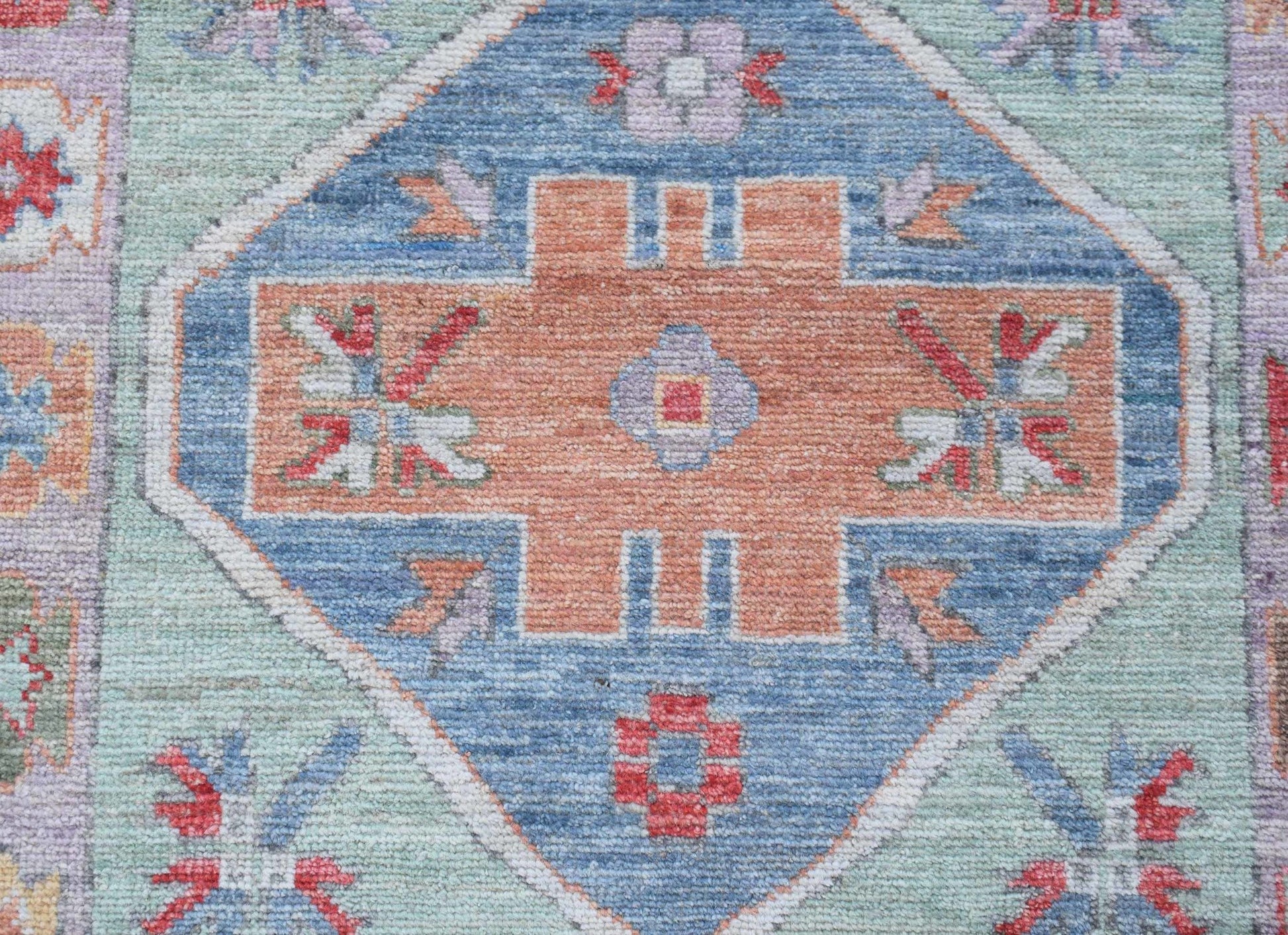 A handwoven wool runner featuring a central orange geometric medallion on a blue and green field.