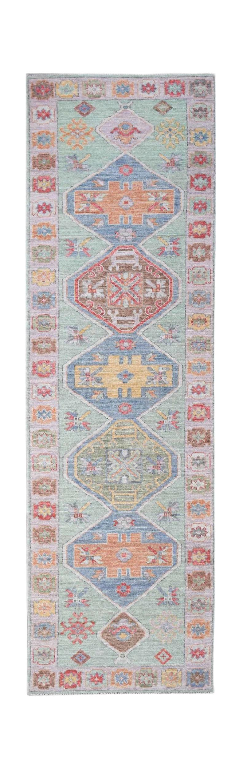 A handwoven wool runner rug featuring a light green field with colorful geometric Oushak motifs.