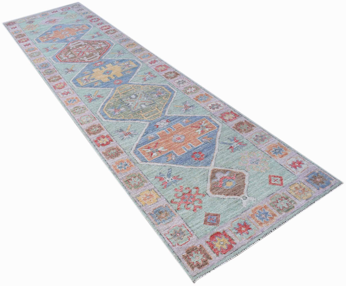 A handwoven wool runner rug featuring a transitional Oushak pattern in soft, multi-colored tones.