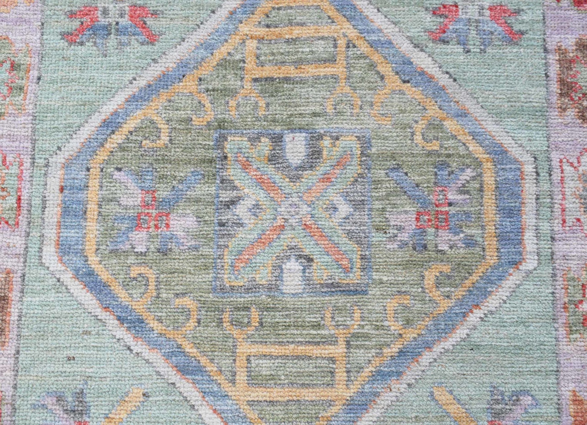 A transitional Oushak runner featuring a central geometric medallion in soft green and blue tones.