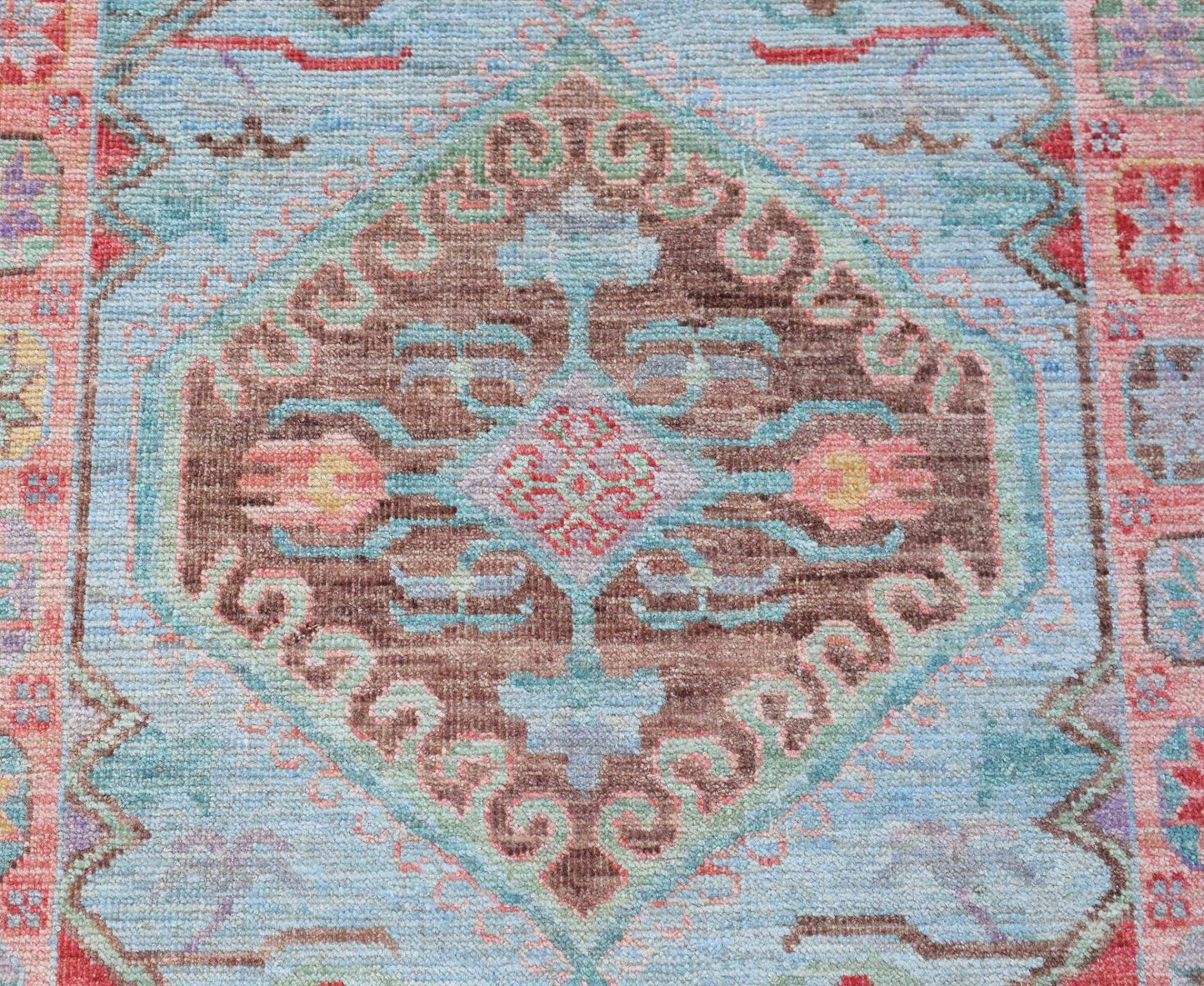 A handwoven transitional Oushak runner featuring a central brown medallion on a light blue field.