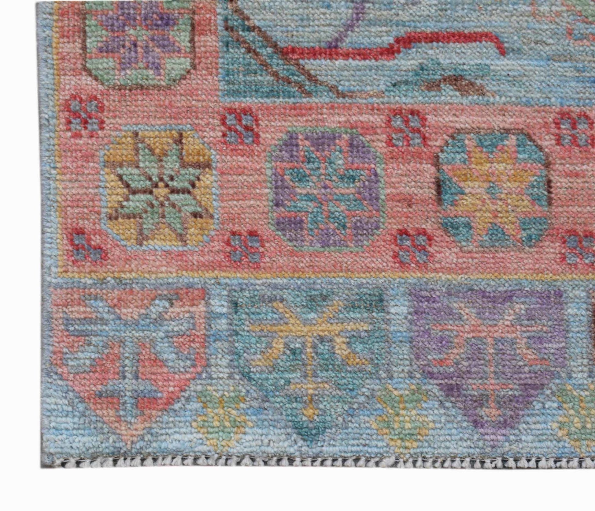 A handwoven wool runner featuring a colorful geometric pattern on a pink and blue background.