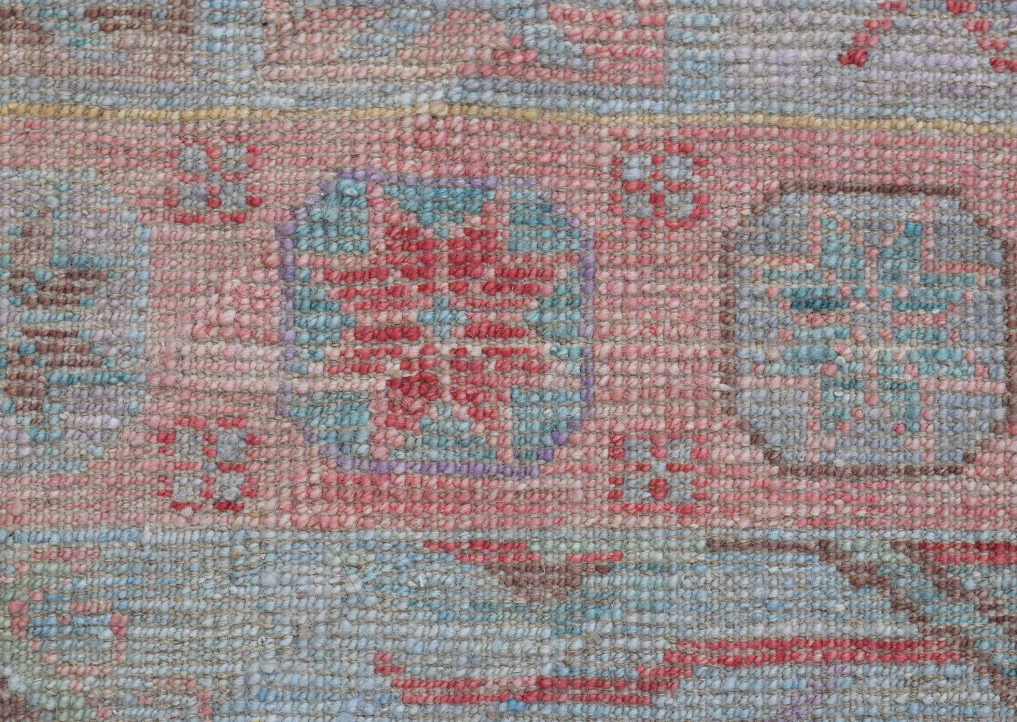 A close-up of a handwoven wool runner featuring a transitional floral pattern in soft pastel tones.