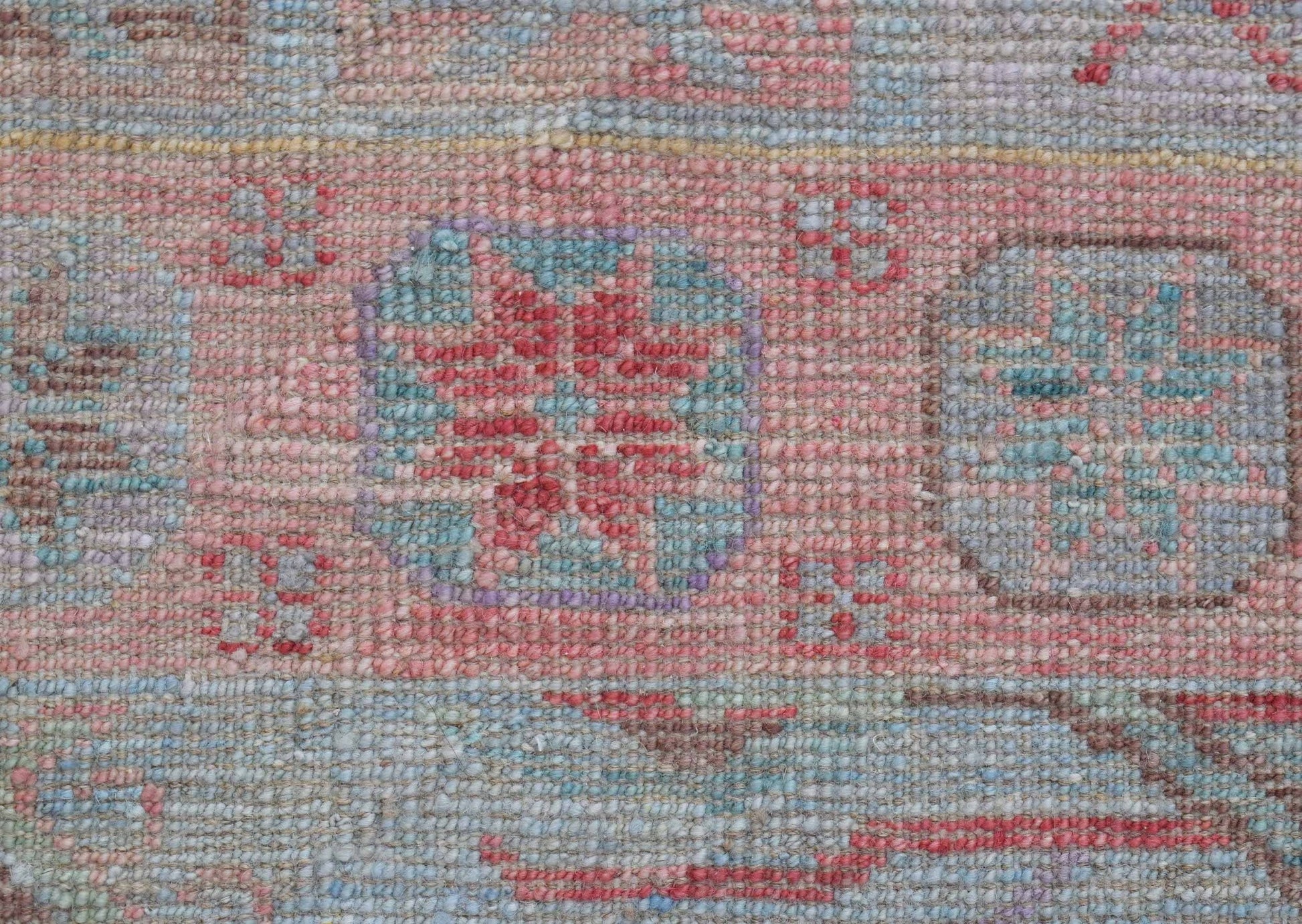 A close-up of a handwoven wool runner featuring a transitional floral pattern in soft pastel tones.