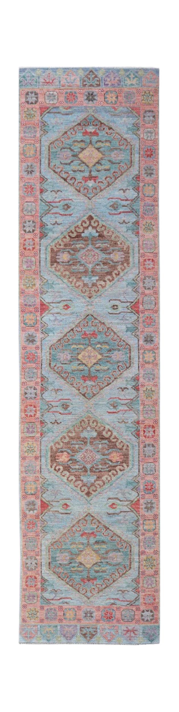 A handwoven wool runner rug featuring a light blue field with repeating geometric floral medallions.
