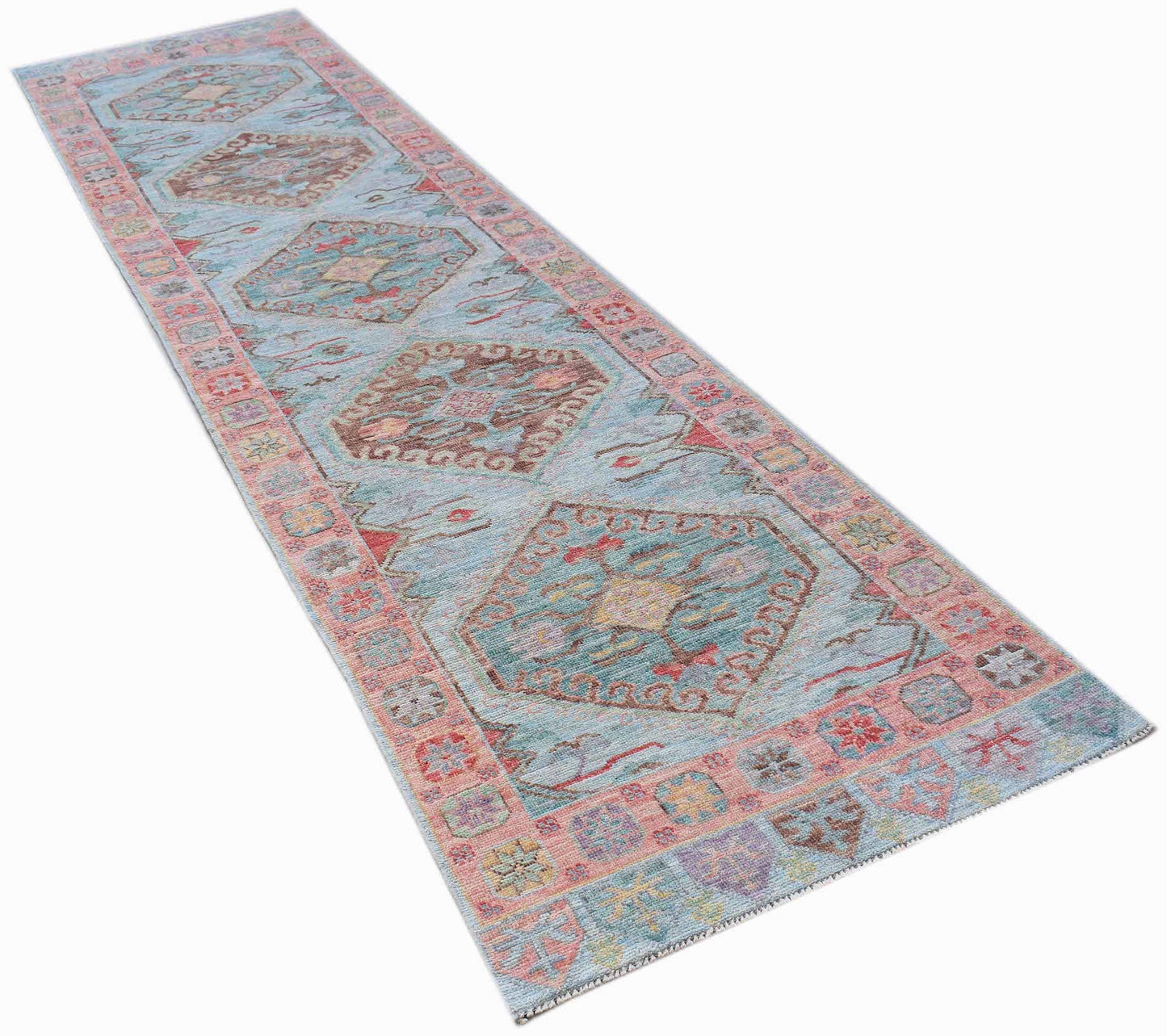 A handwoven wool runner rug featuring a light blue field with repeating geometric floral motifs.