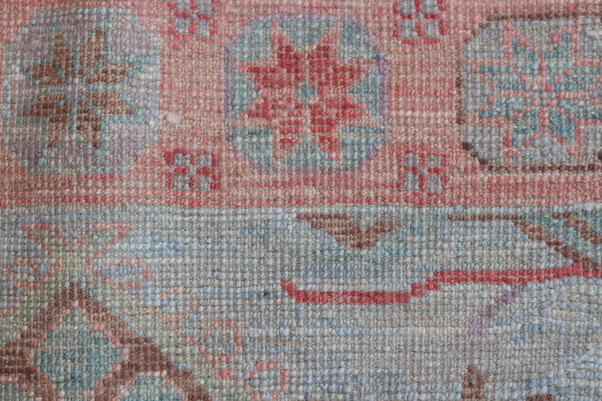 A close-up of a handwoven wool runner rug featuring a transitional floral pattern in soft tones.