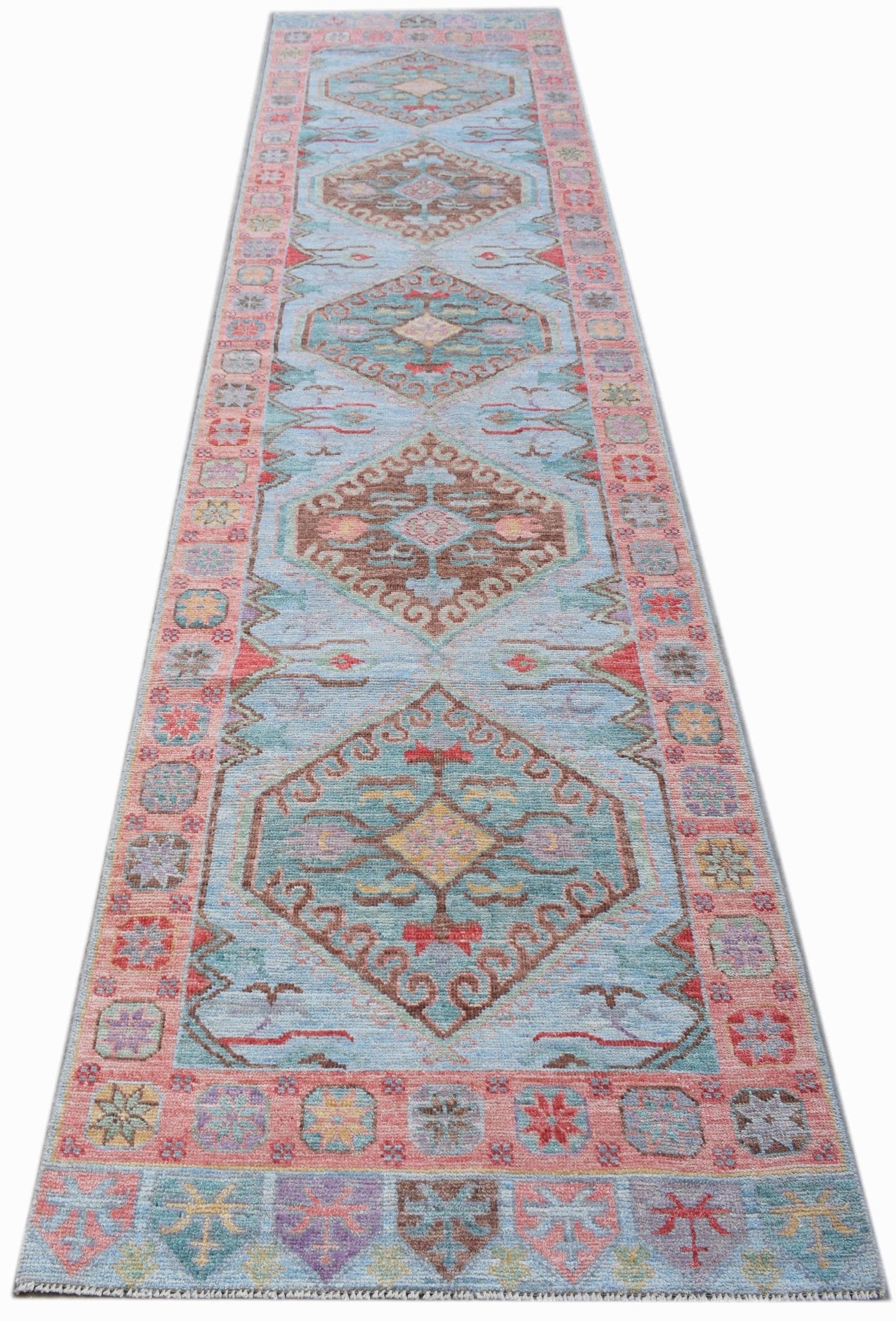 A handwoven wool runner rug featuring a light blue field with repeating geometric floral medallions.