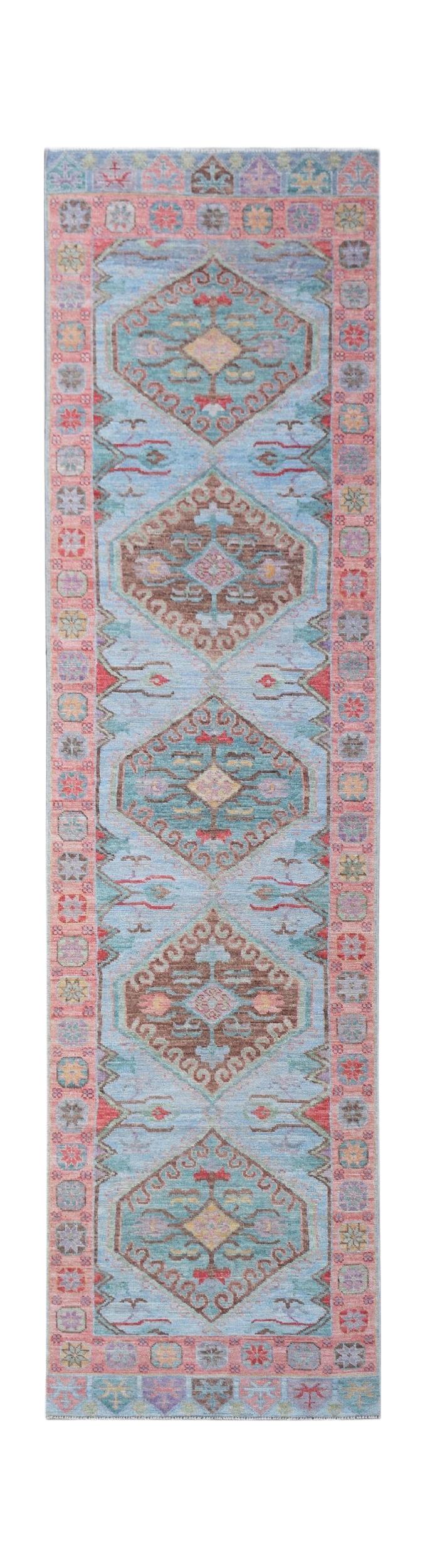 A handwoven wool runner rug featuring a light blue field with repeating geometric floral medallions.