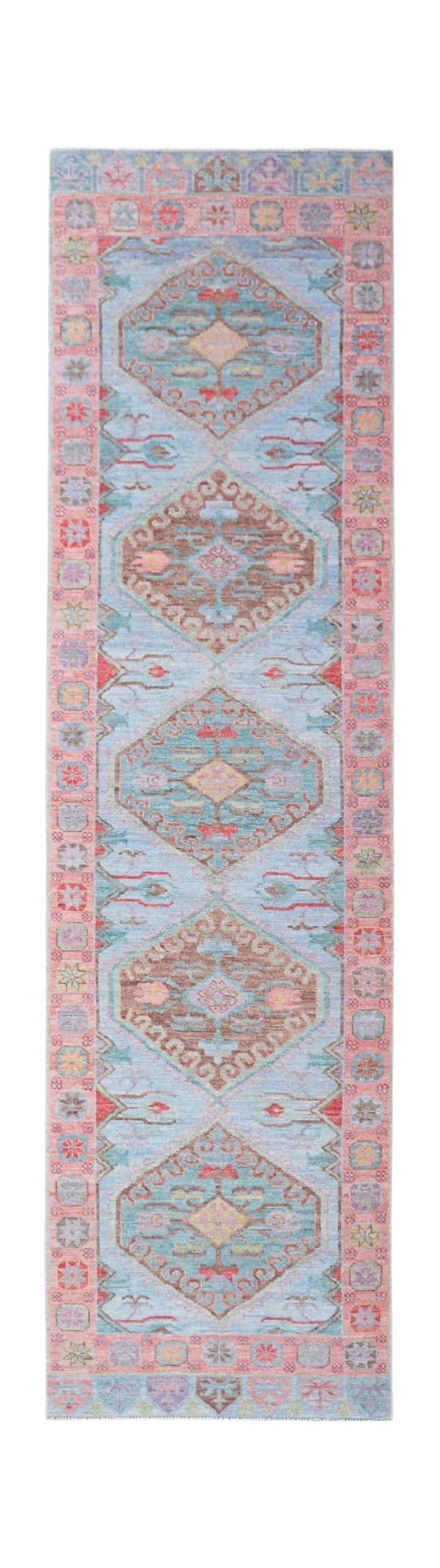 A handwoven wool runner rug featuring a light blue field with repeating geometric floral medallions.