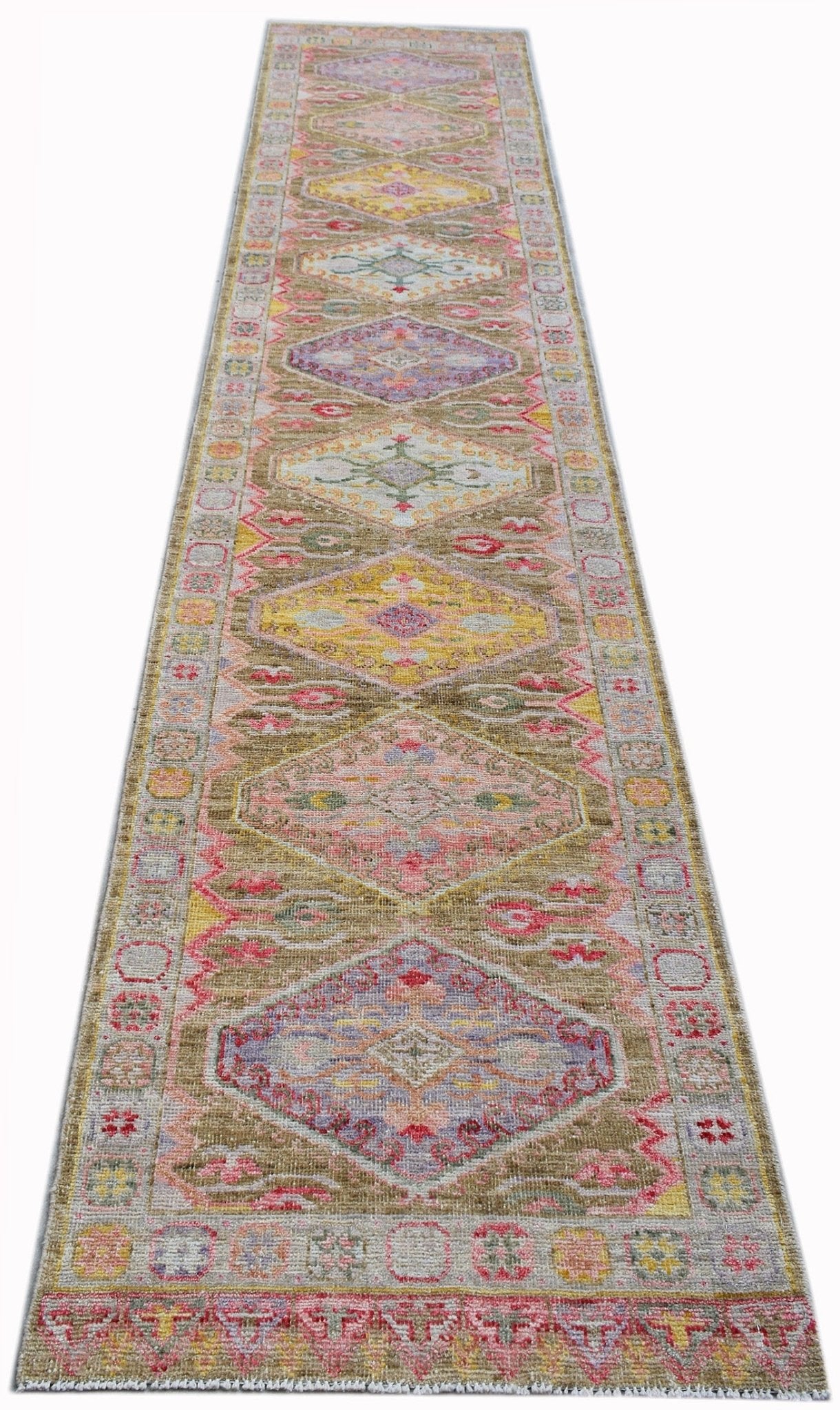A handwoven wool runner rug featuring a series of colorful diamond medallions on a tan background.